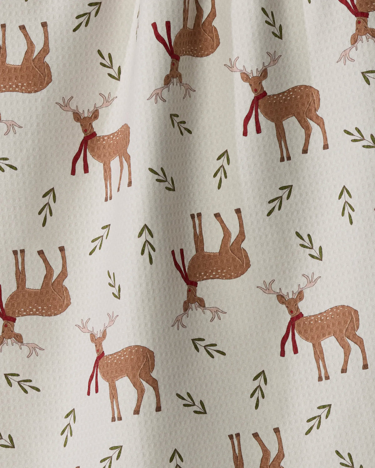The “Winter Reindeer” tea towel by Geometry features a white textured background adorned with brown reindeer wearing red scarves, scattered green sprigs, and playful directional patterns—combining quick-drying utility with festive style.
