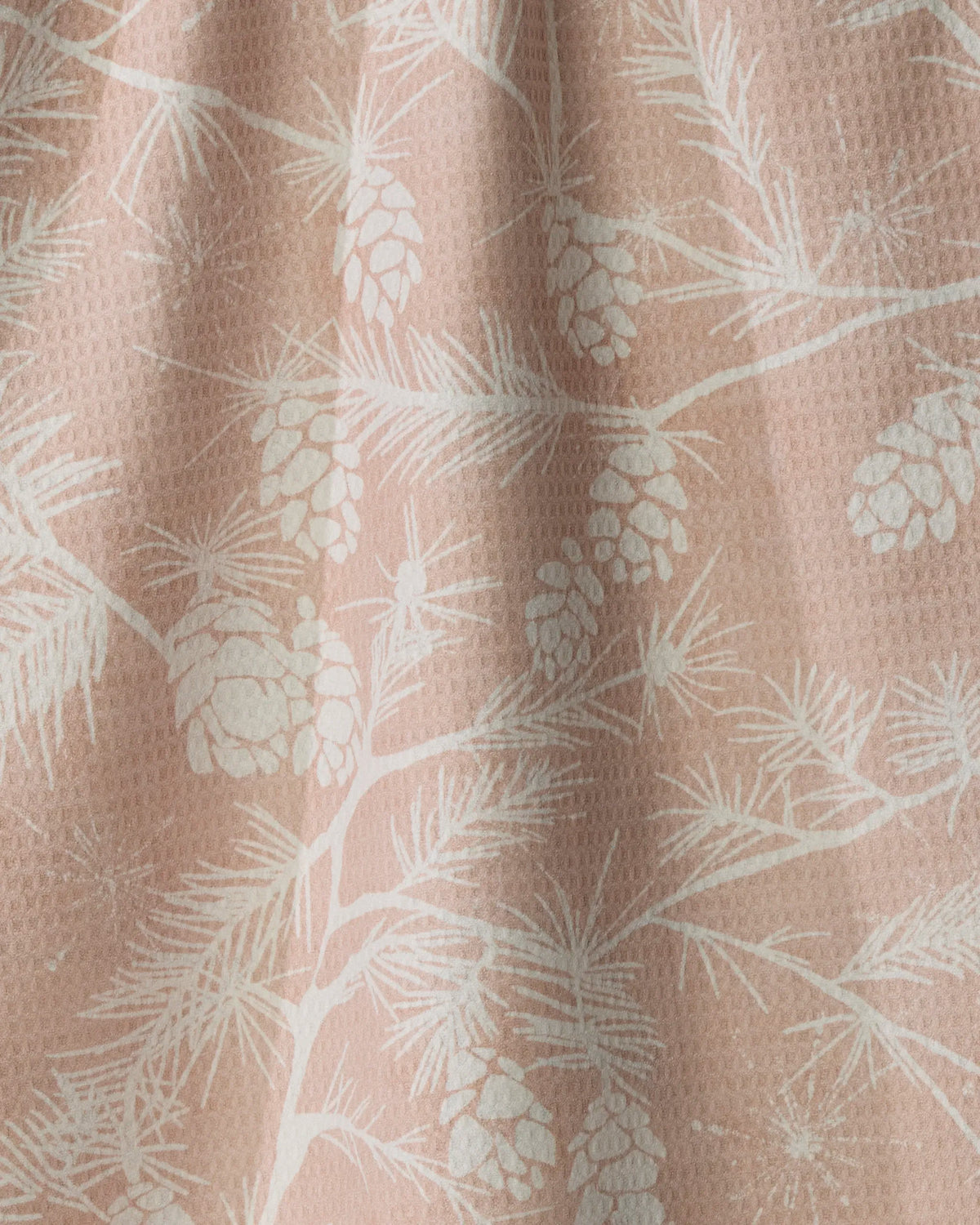 A close-up of the Woodland Calm tea towel by Geometry showcases its textured fabric, adorned with a white pinecone and branch pattern on a light pink background—this quick-drying towel brings together beautiful design and everyday practicality.