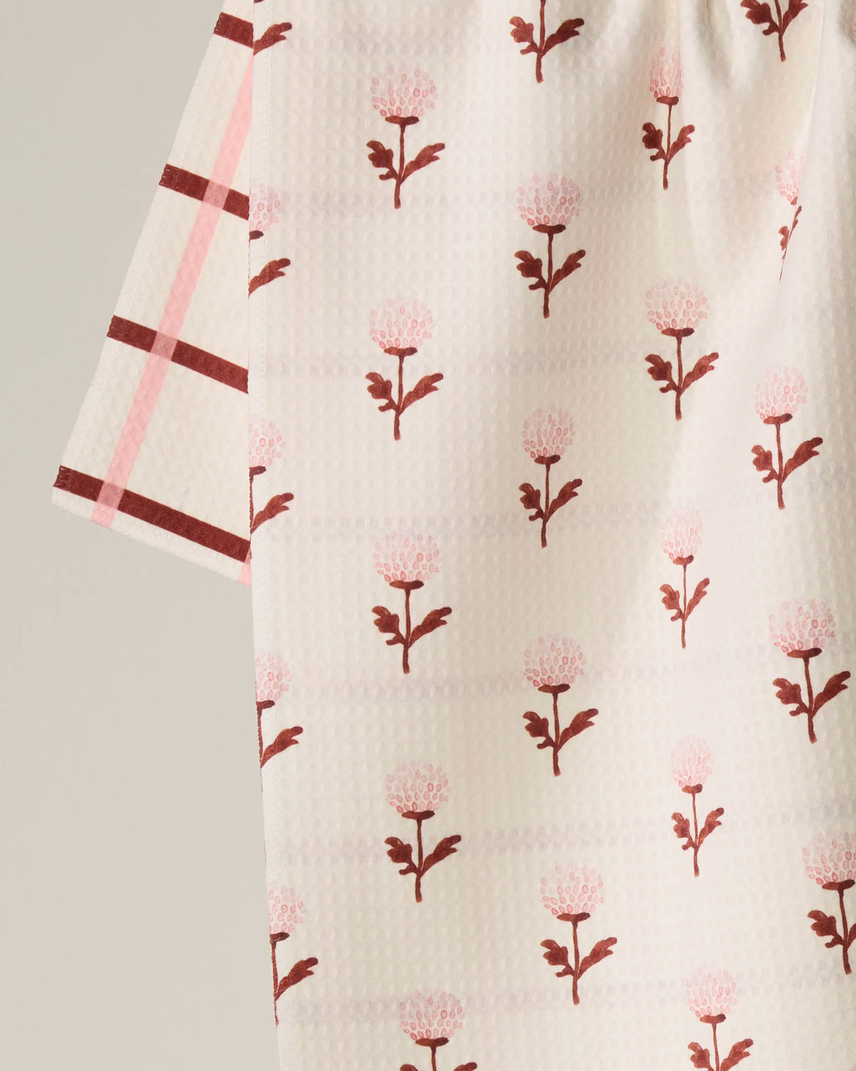 A close-up of Geometry’s Fleur fabric showcases a pink and red floral pattern, complemented by a contrasting sleeve in pink, red, and white plaid—expertly crafted from recycled materials for an eco-friendly touch.