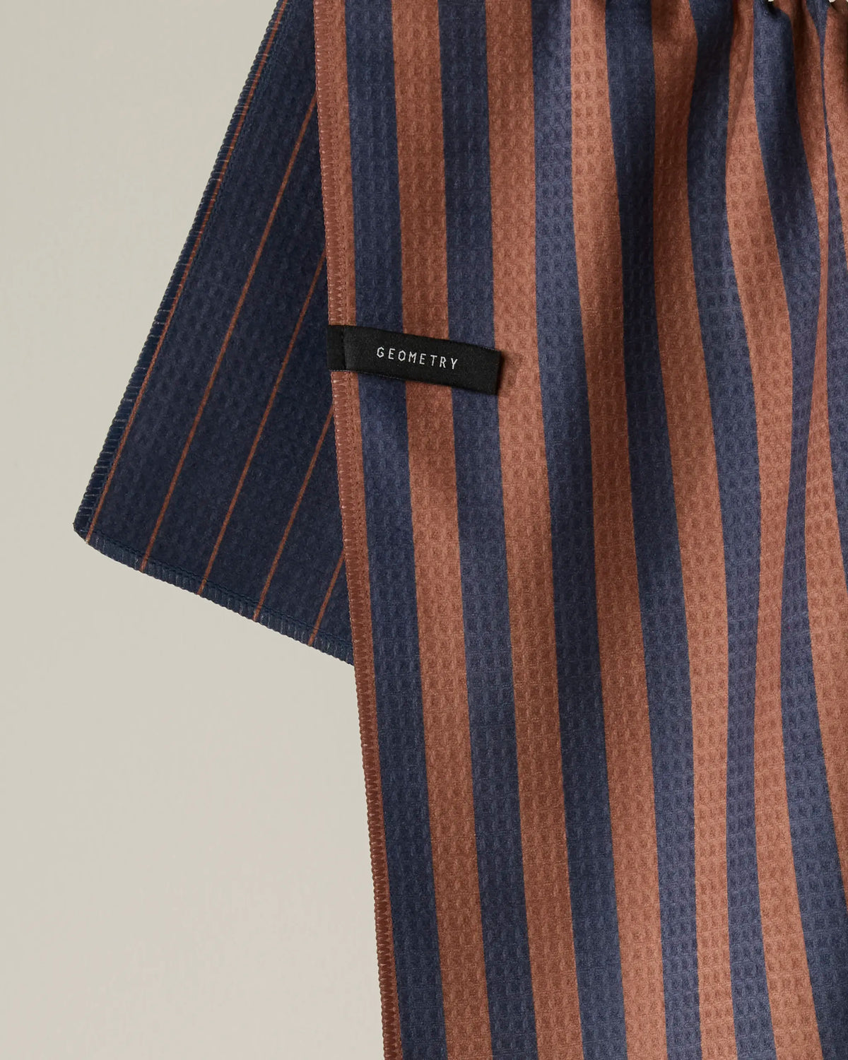 A close-up of Geometry’s Midnight Stripe fabric, featuring vertical brown and navy blue stripes with a black Geometry label. The material has a subtly textured pattern and is designed as a quick-drying tea towel, making it ideal for everyday kitchen use.