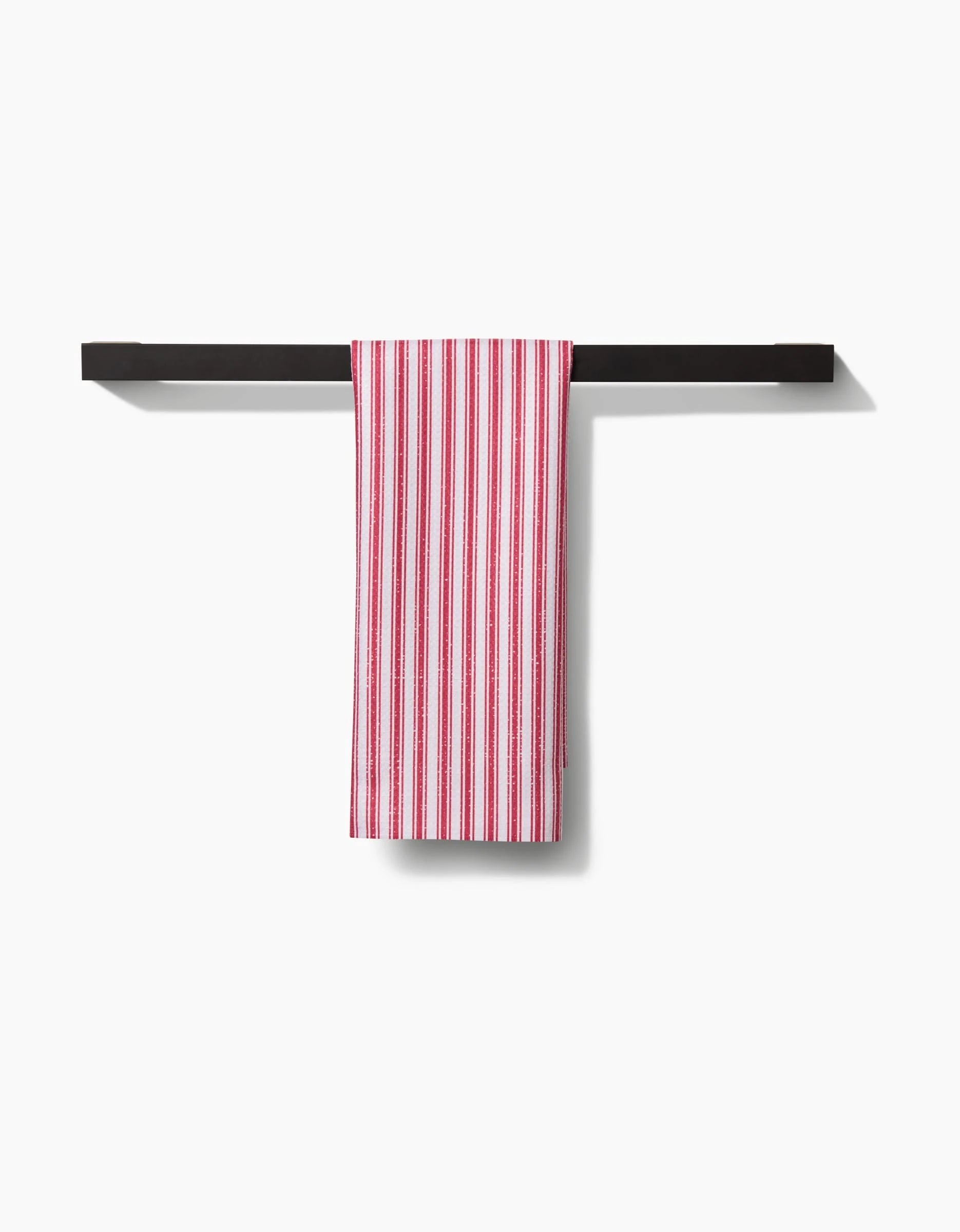A Becki Owens Red Ticking tea towel, crafted from Geoweave fabric and featuring red vertical stripes, hangs neatly over a black towel bar against a plain white background.