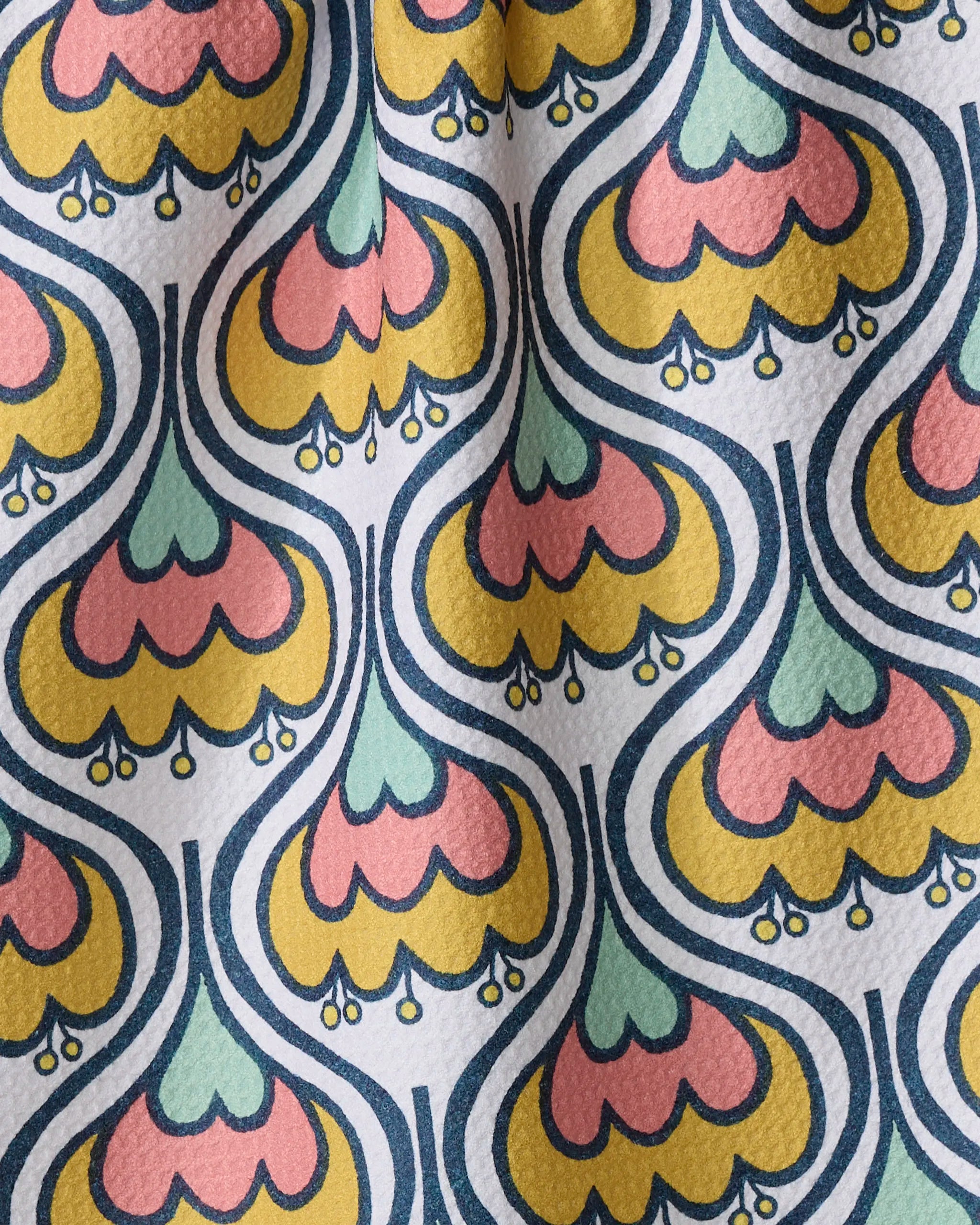 The Renee Fly 70s Floral kitchen towel features a colorful, retro-style pattern with yellow, pink, and teal petals outlined in blue on textured white recycled fabric.
