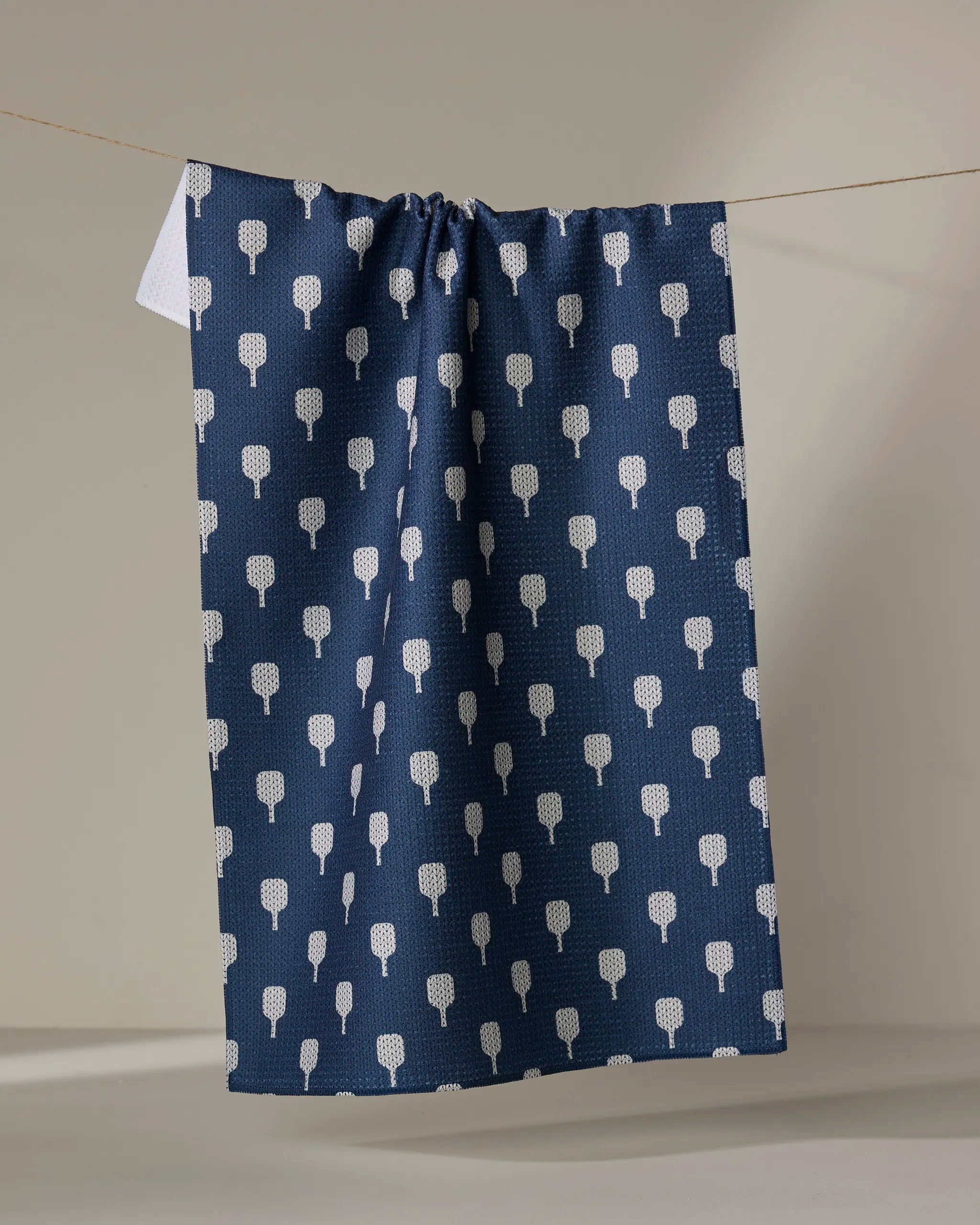 The Modern Dad's "Mr. Pickler" is a dark blue kitchen tea towel with a repeating white tree pattern, made from recycled materials, shown hanging on a clothesline against a simple, neutral background.