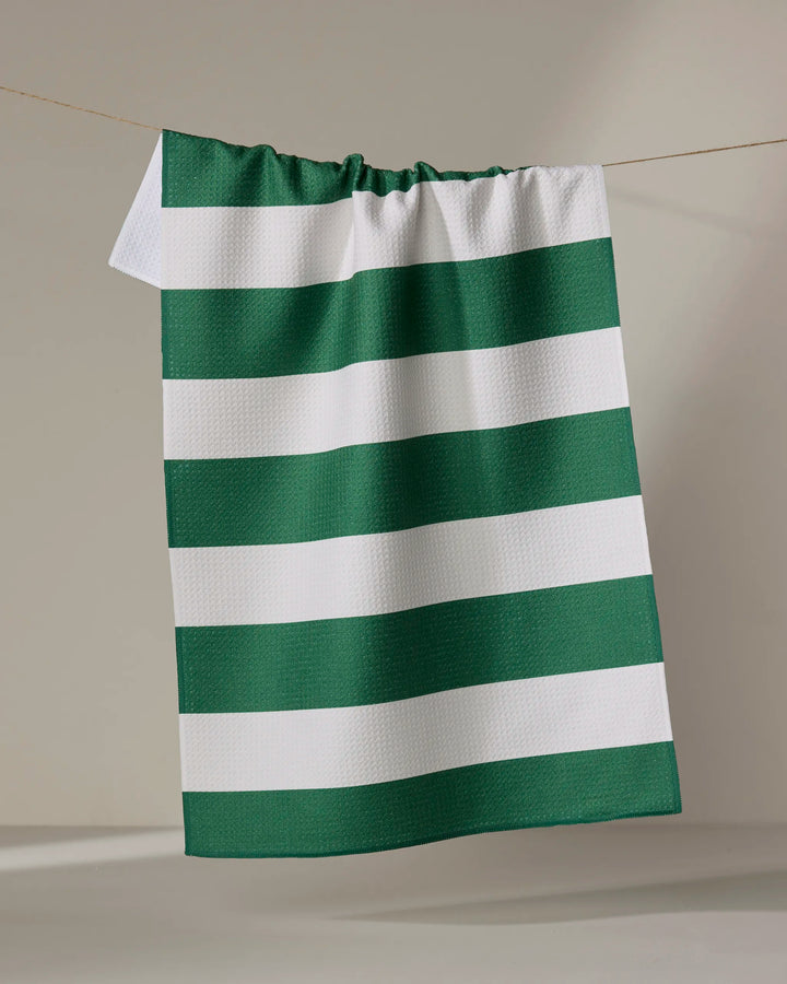 The Modern Dad’s “Mr. Day On The Green” kitchen towel, featuring green and white horizontal stripes, hangs on a string against a plain, light-colored background.