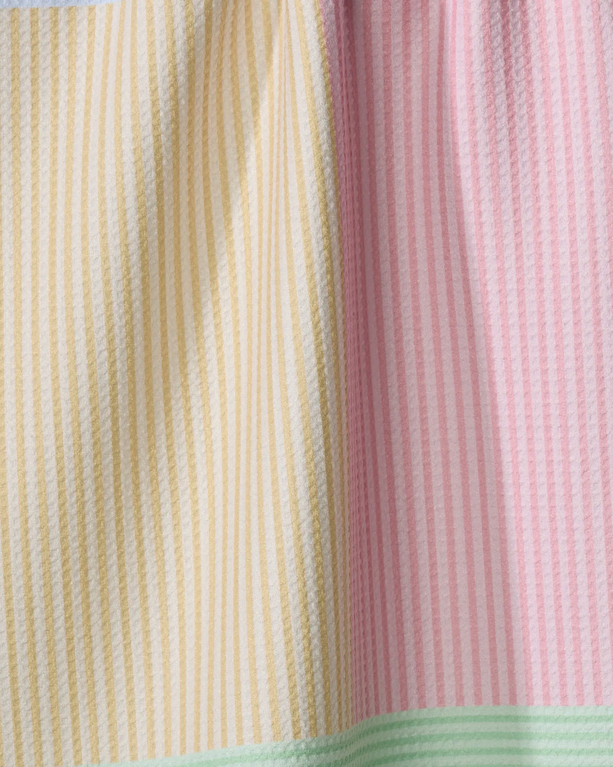 A close-up of The Modern Dad’s Mr. Fun Stripes tea towel shows vertical yellow and pink stripes with a seam, plus a mint green stripe at the bottom. This ultra-absorbent, soft towel has a textured look and is crafted from recycled materials.