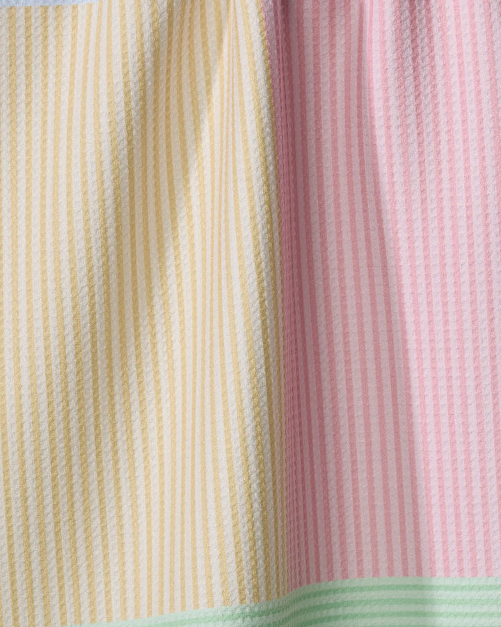 A close-up of The Modern Dad’s Mr. Fun Stripes tea towel shows vertical yellow and pink stripes with a seam, plus a mint green stripe at the bottom. This ultra-absorbent, soft towel has a textured look and is crafted from recycled materials.