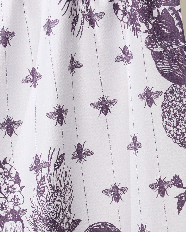 A close-up of the Geometry "Abeilles Noires" tea towel, showcasing its charming white fabric with a purple floral and bee print, featuring rows of bees and detailed flowers for a stylish, nature-inspired kitchen accent.