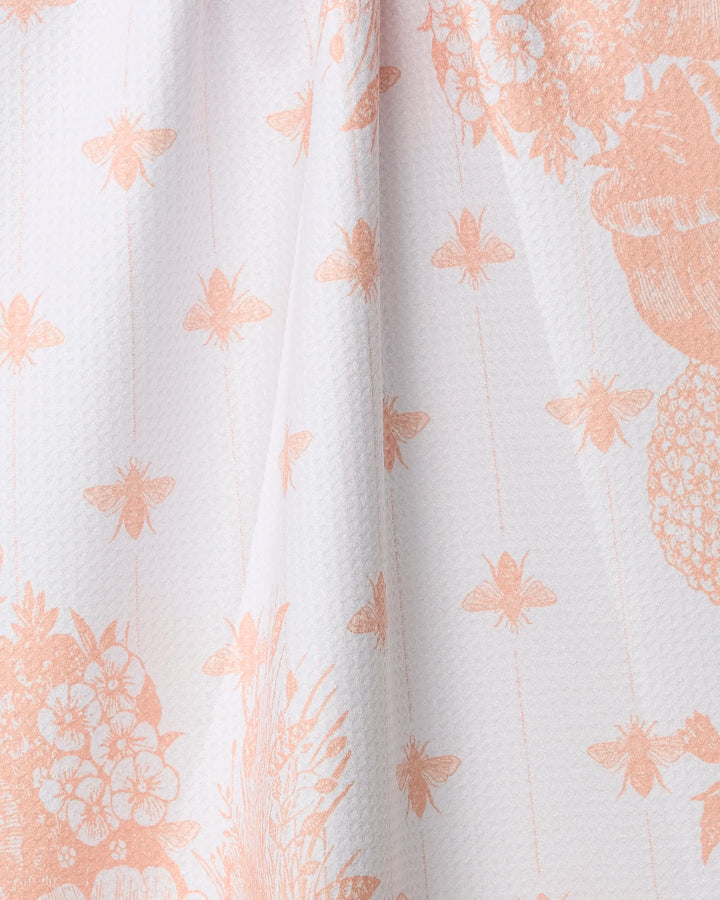 Close-up of Geometry’s Abeilles kitchen towel, featuring a peach pattern of bees, flowers, and plants on recycled material for a soft, nature-inspired look.