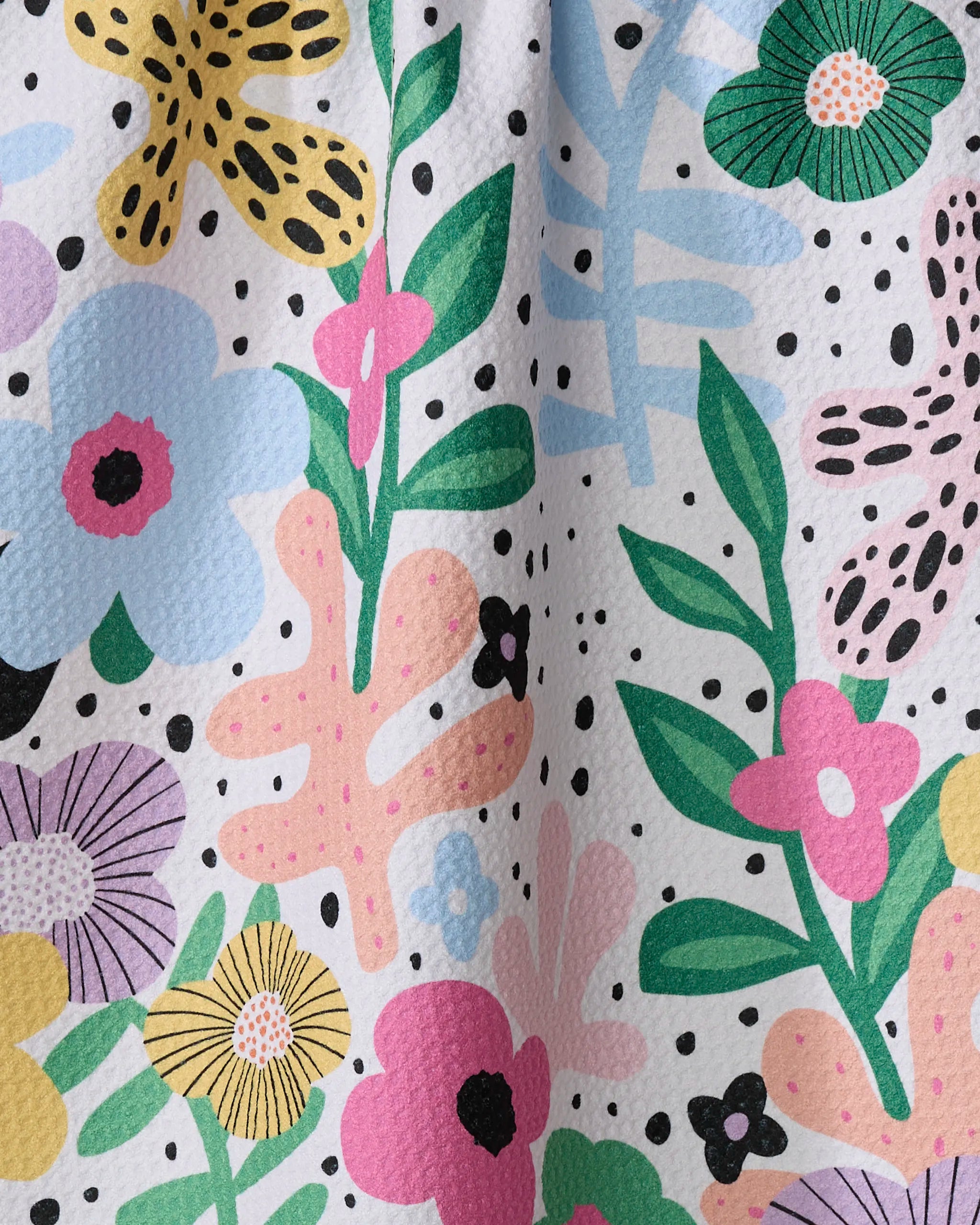 A close-up of the Marina Solodka "Abstract Botanicals" Geoweave tea towel, featuring a colorful floral pattern with blue, pink, yellow, and green flowers and leaves plus scattered black dots on a white background.