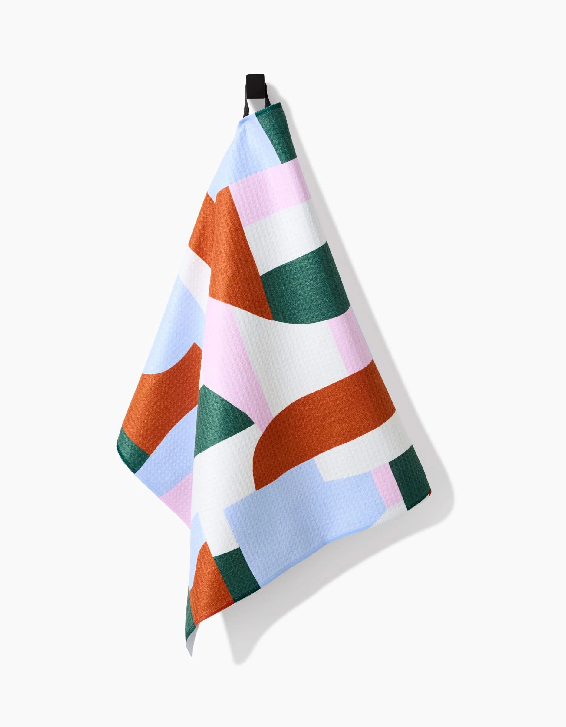 The Claire Iglesias Abstract Collage tea towel, made from recycled materials, features an abstract geometric pattern in green, rust, blue, pink, and white and hangs from a black loop against a white background.