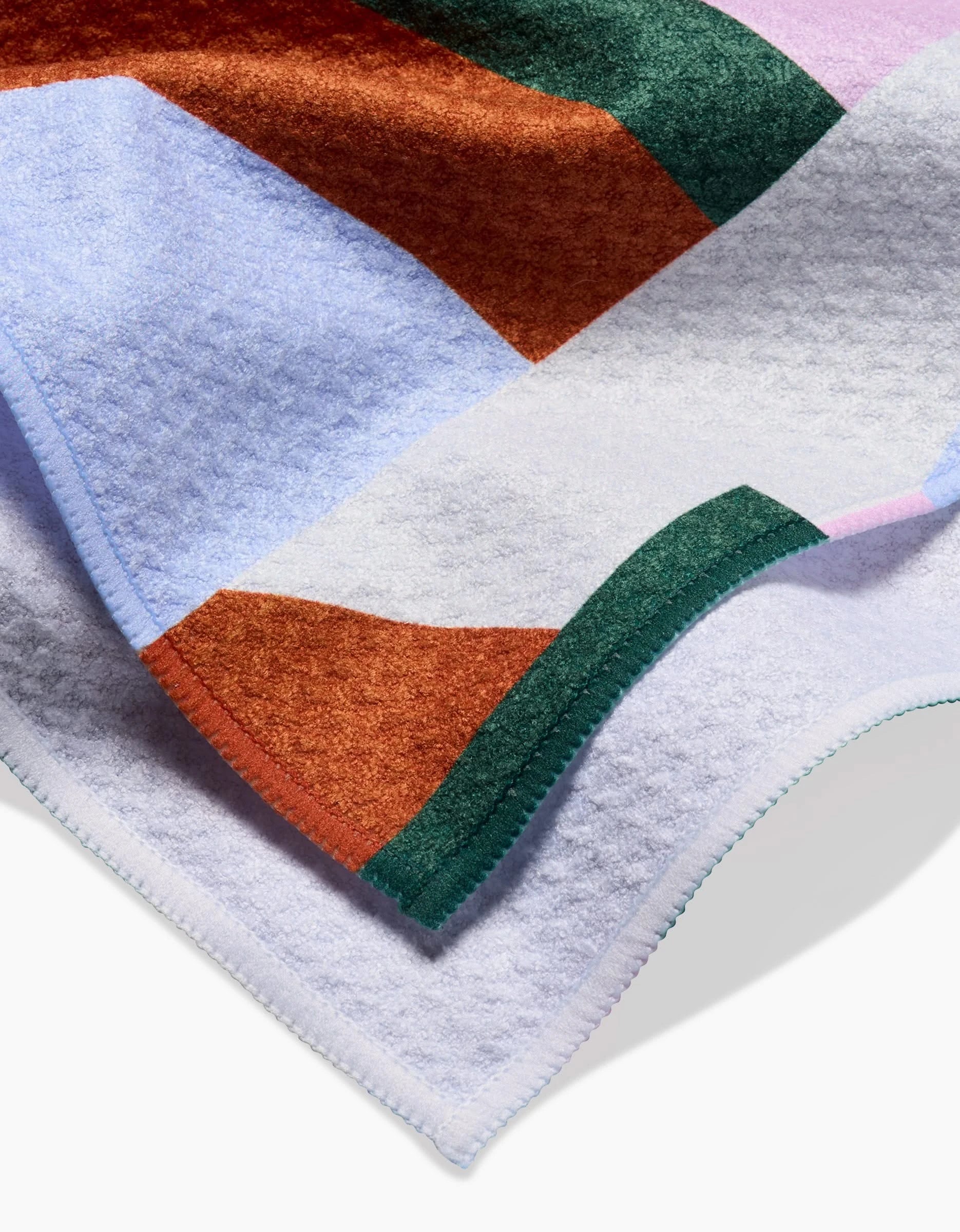 A close-up of Claire Iglesias’s Abstract Collage blanket, crafted from soft Geoweave fabric, featuring a geometric pattern in purple, orange, green, and white with neatly stitched edges.