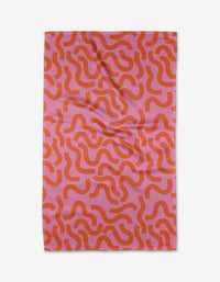 The Abstract Snake by Jennifer Bouron is a rectangular, recycled kitchen towel with an abstract pattern of wavy orange lines on a pink background, shown flat against a white surface.