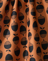 The Geometry Acorn Noir kitchen tea towel features a textured orange fabric with evenly spaced rows of black acorns and leaves. Gentle folds add shadows and highlights to its ultra-absorbent design.