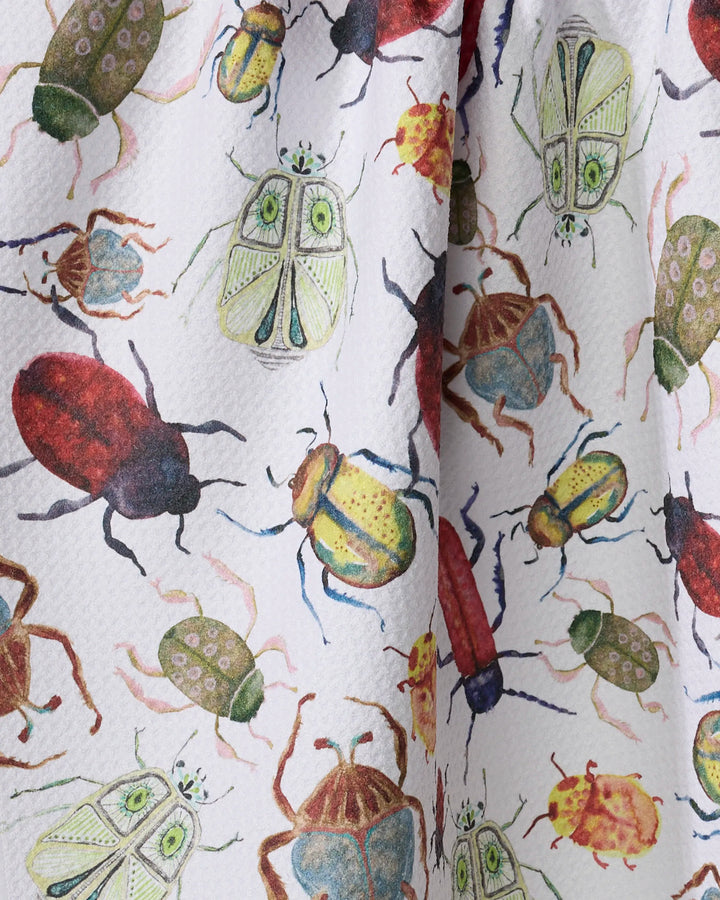 A close-up of the Taryn Brennan "African Beetles" tea towel, showcasing a colorful, detailed pattern of illustrated beetles and insects on a white background.