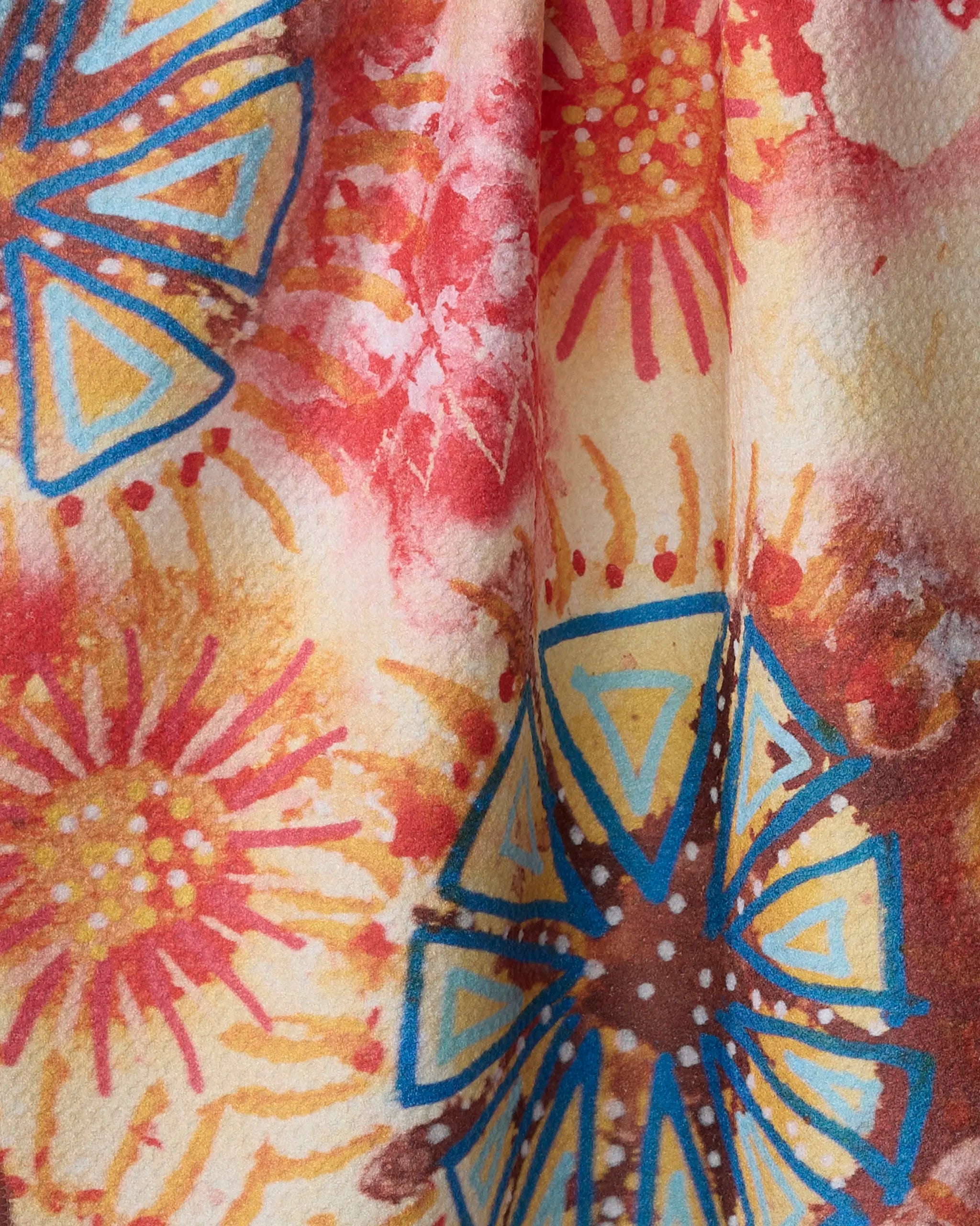 Close-up of Taryn Brennan’s African Loose Circles eco-friendly kitchen towel, featuring a vibrant pattern with red, yellow, and blue abstract floral and geometric shapes—circular bursts and triangles on a light background.
