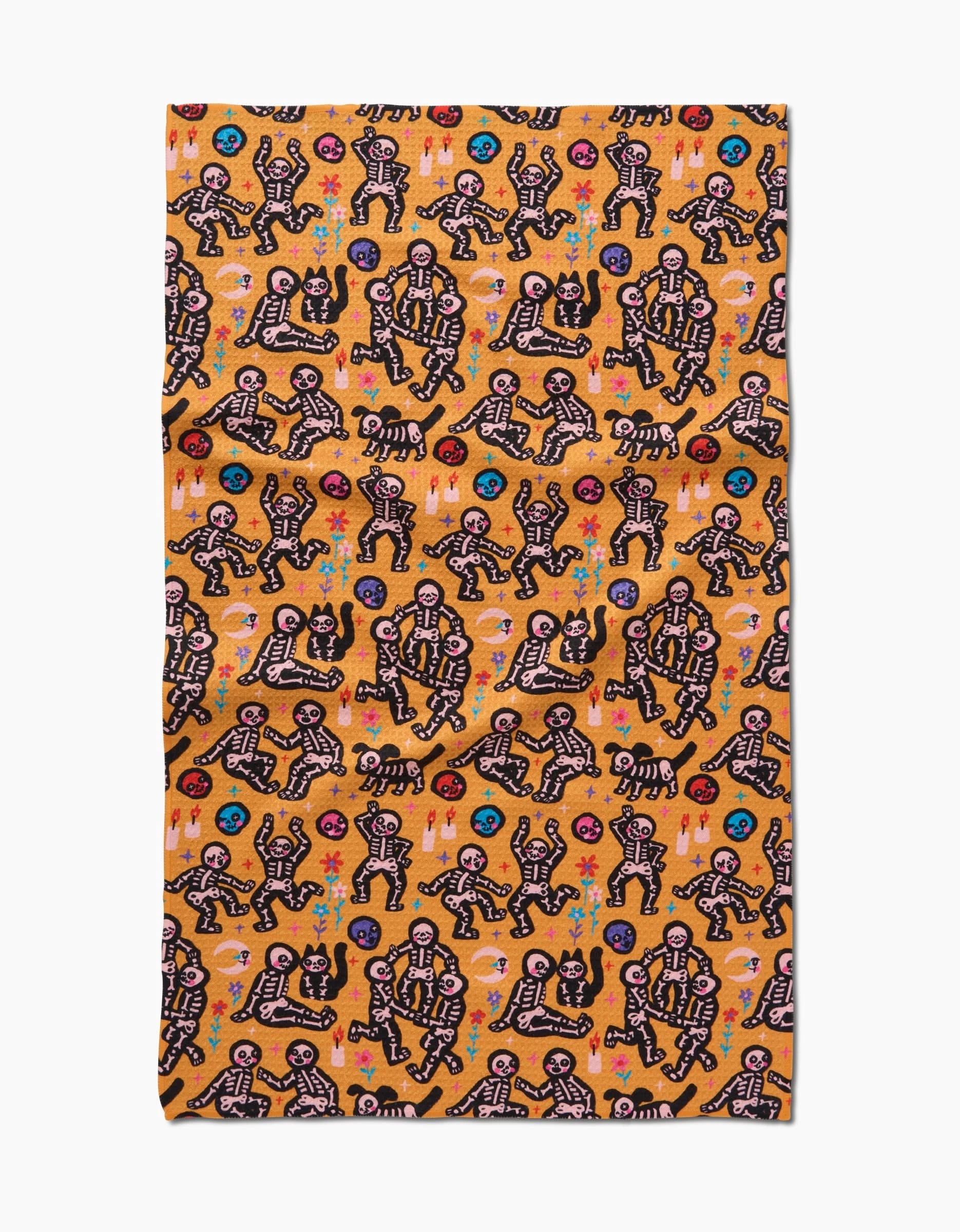 The After Party tea towel by So Lazo features a bold orange backdrop with black skeletons dancing and playing instruments, accented by colorful flowers and geometric shapes. Made from quick-drying recycled materials.