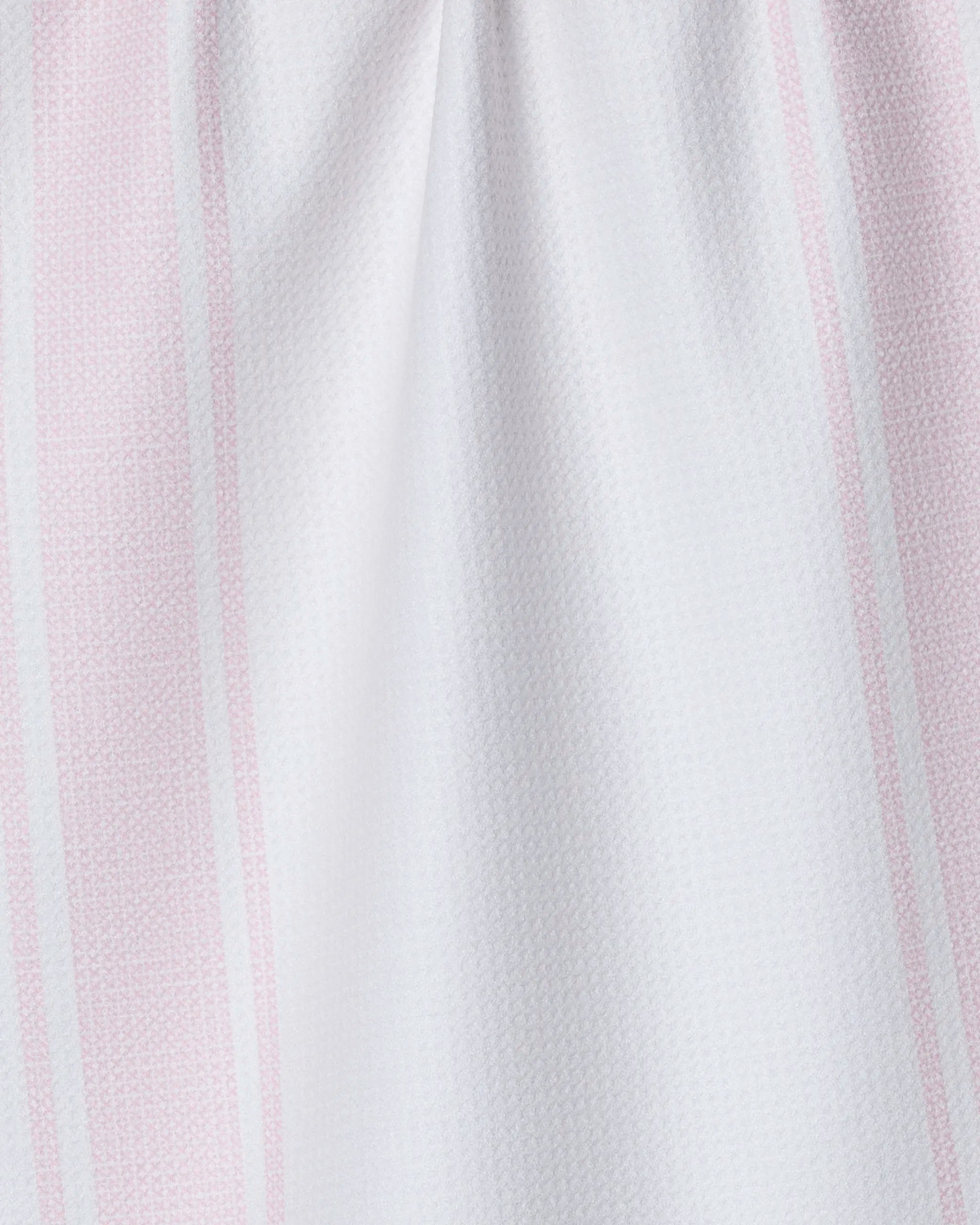 A close-up of Geometry's All For You kitchen towel, crafted from recycled materials, features white fabric with vertical light pink stripes and a subtle textured pattern, its gentle folds creating soft shadows.