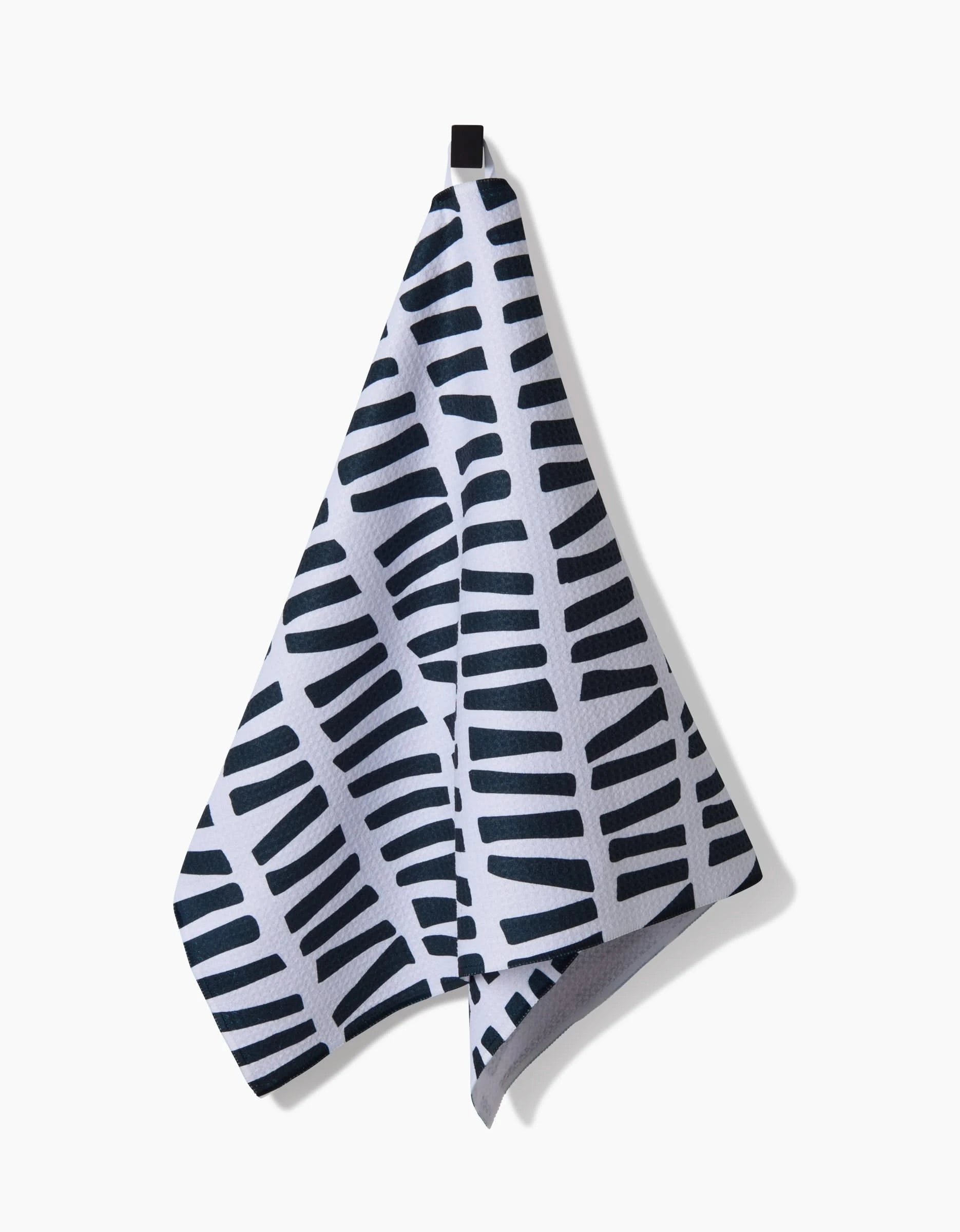 The GEOMETRY All Lined Up tea towel, ultra-absorbent and white with a black geometric stripe pattern, hangs from a black loop against a plain white background.