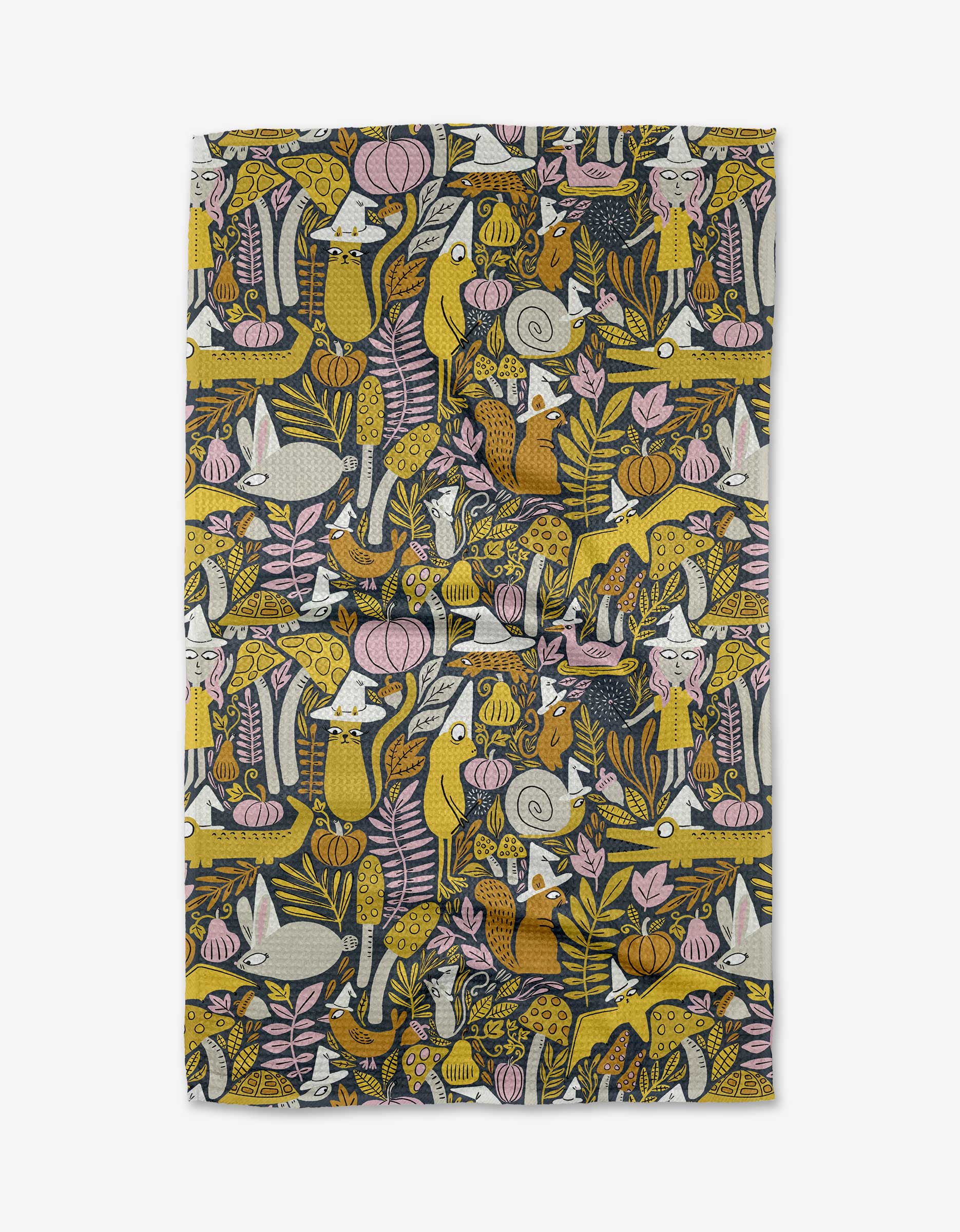 The All The Little Witches tea towel by Amy MacCready features a whimsical forest scene with foxes, birds, mushrooms, and flowers in yellow, pink, gray, and white on a dark background.
