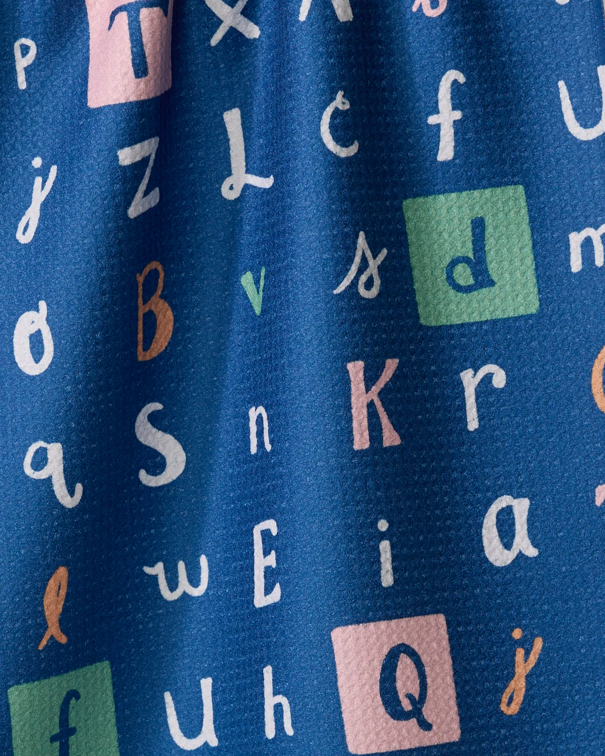The "Alphabet" tea towel by Amy MacCready is blue, made from quick-drying recycled materials, and features assorted colorful letters in various fonts with pastel squares highlighting some letters.