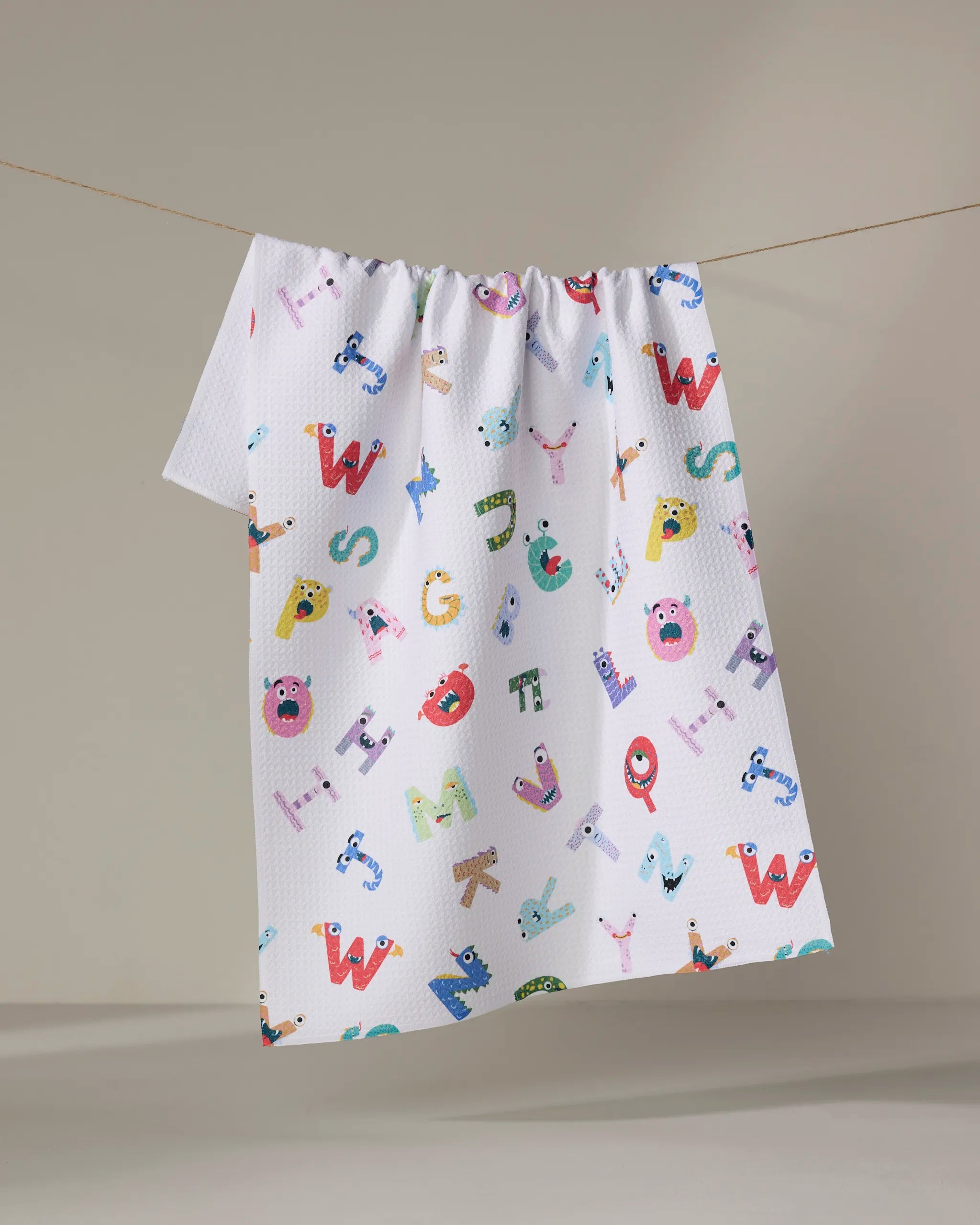 The Alphabet Monsters tea towel by Vaishali Design Studio features playful alphabet letters with cartoon faces on white ultra-absorbent recycled fabric, adding eco-friendly charm and color to any minimal space.