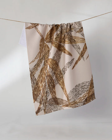 The Geometry Amber Wildflower recycled kitchen towel, featuring a brown and tan abstract brushstroke pattern, hangs on a thin string against a plain white background.