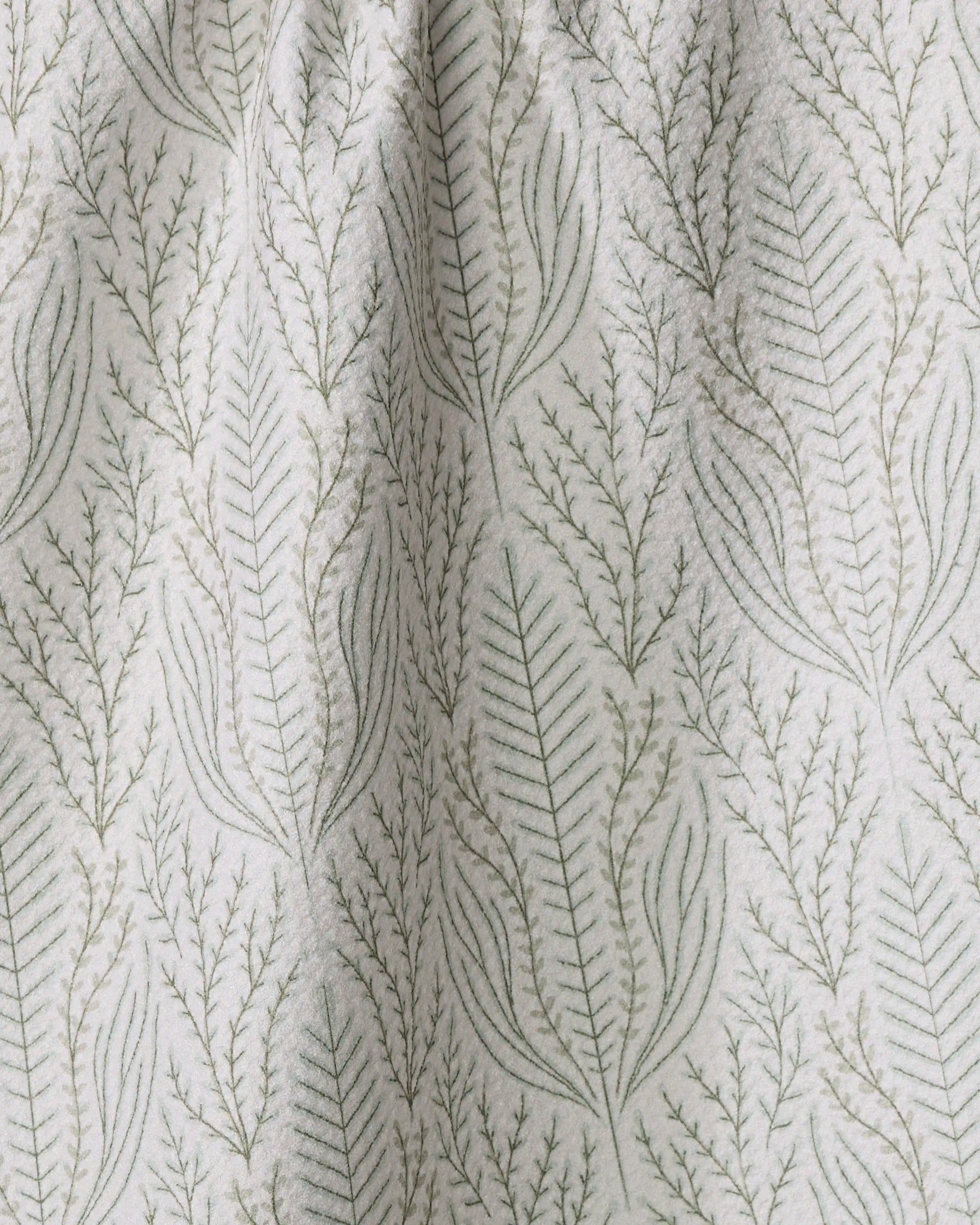 A close-up of the Amberlin tea towel by Amy MacCready, showcasing a subtle botanical design with delicate green leafy branches arranged vertically on a light background.