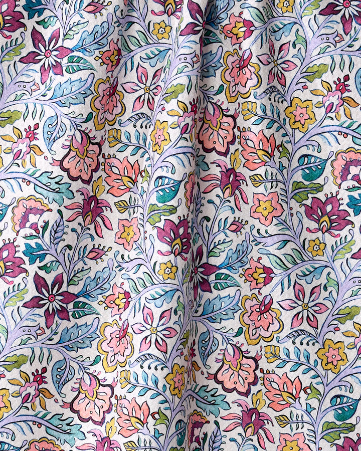 A close-up of the eco-friendly "Amethyst" kitchen towel by Maayan Alper-Swan, showcasing its colorful floral pattern with pink, yellow, and purple flowers and green-blue leaves softly draped on a light background.