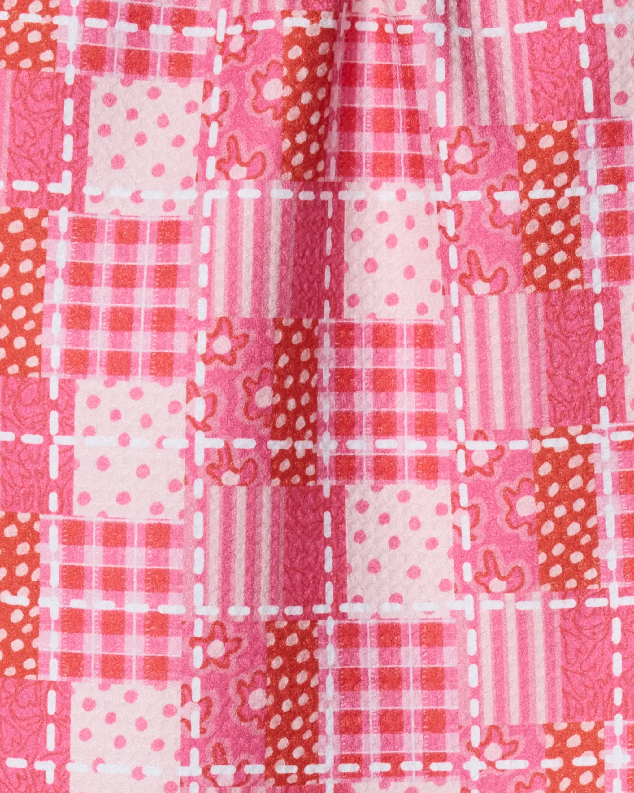 A close-up of Geometry’s Amor Amor bar towel showcases a patchwork pattern in pink and red with polka dots, stripes, florals, and checks outlined by white dashed lines. Made from ultra-absorbent recycled materials.