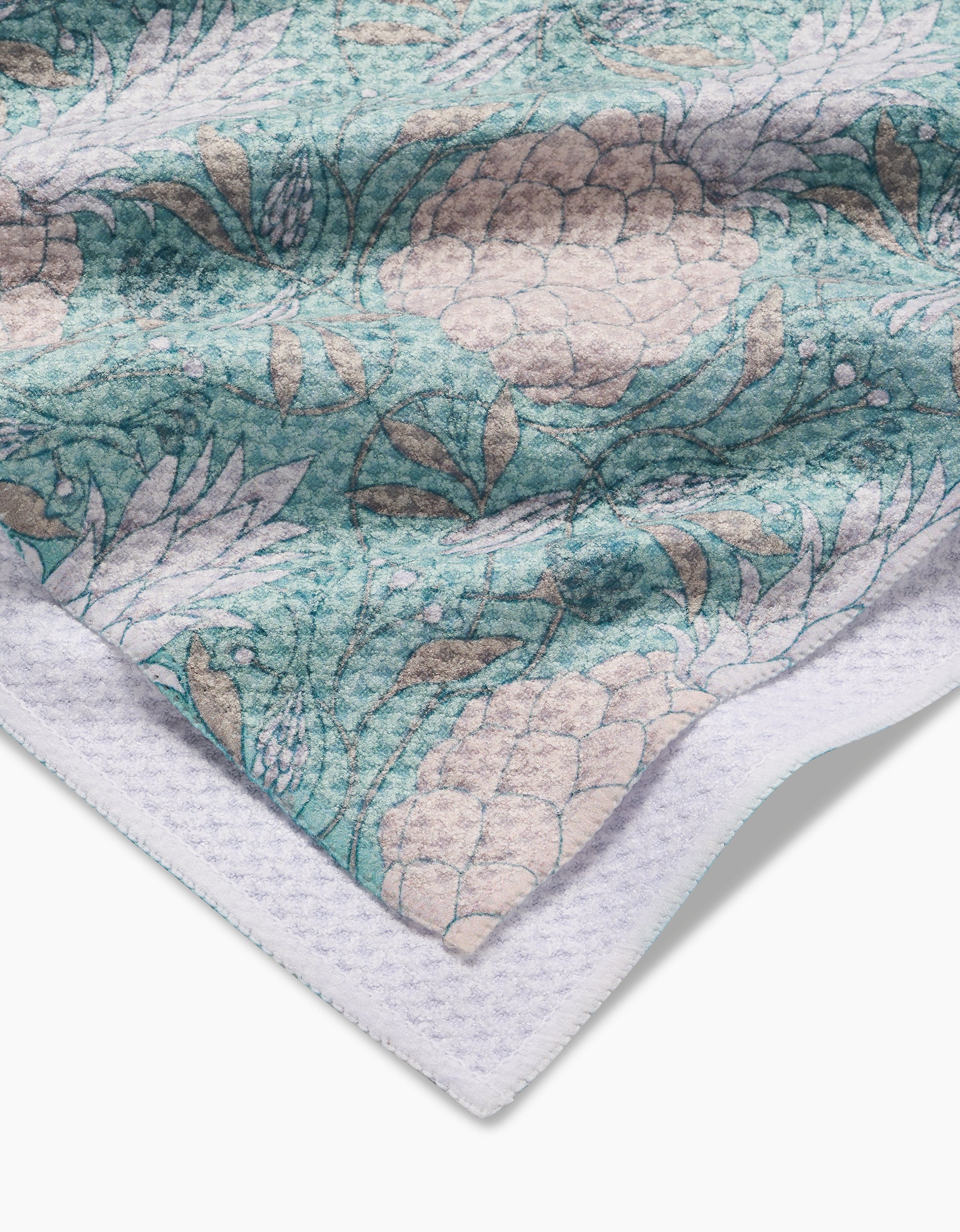 A close-up of the Andre fabric by Amy MacCready shows a textured surface in teal, beige, and white with a floral pattern of large flowers and a waffle-like white border along the bottom left edge.
