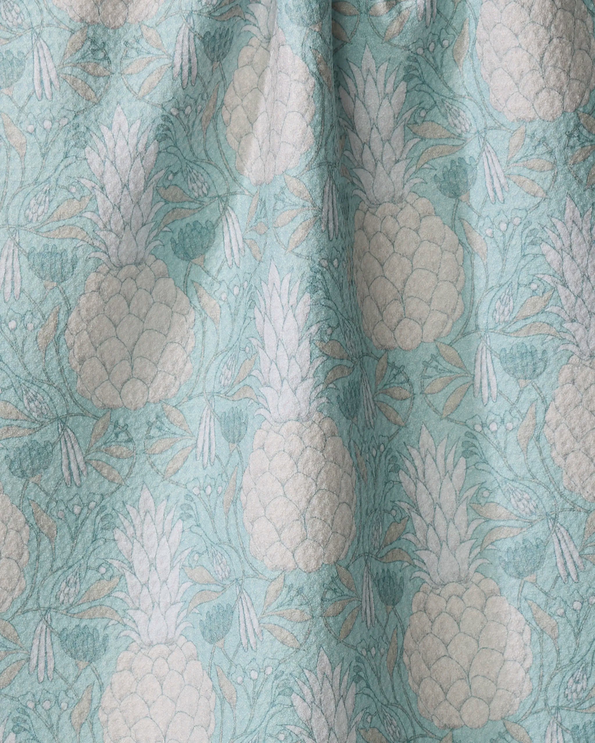 The Andre by Amy MacCready features light blue fabric with white pineapples and leaves. Made from quick-drying recycled materials, the repeating design and gentle folds create subtle texture and shadow on the surface.