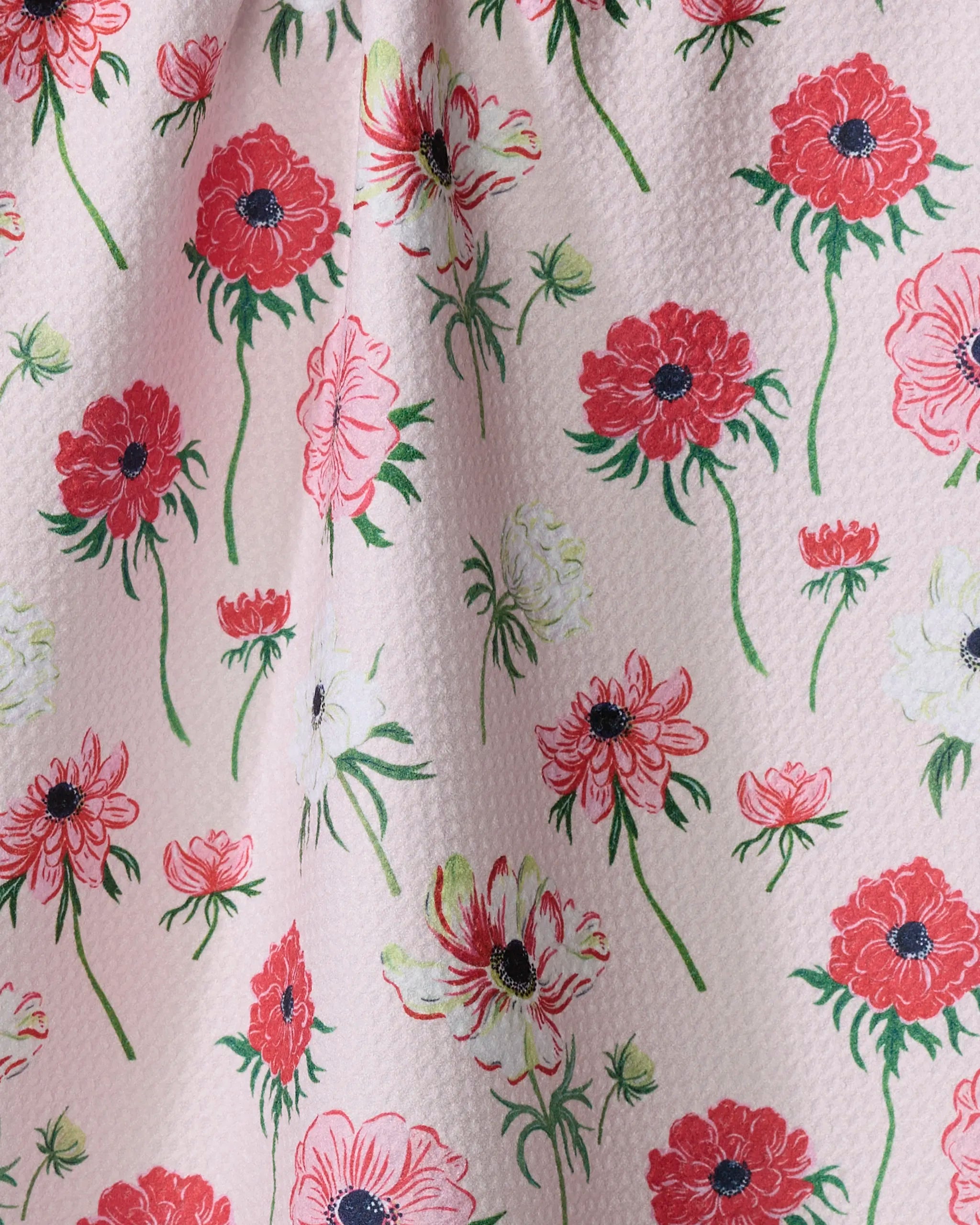 The Anemone Garden Flowers tea towel by Linda Fox features a light pink, textured design made from recycled materials, adorned with lively red, pink, and white flowers plus charming green stems for a cheerful, ultra-absorbent touch.
