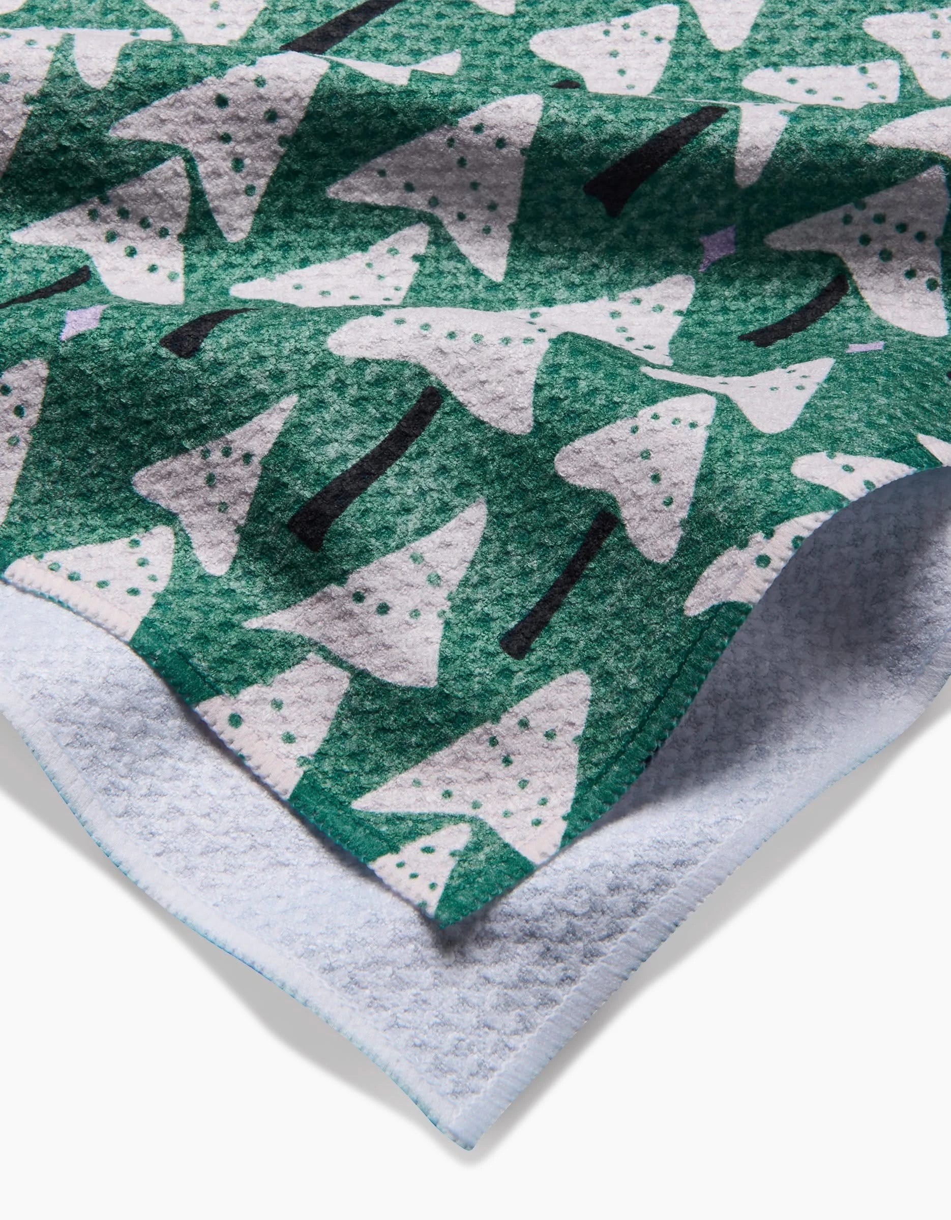 A close-up of the Angelina recycled kitchen towel by Amy MacCready, featuring white and dotted Christmas trees on green, with a textured, light-colored underside.