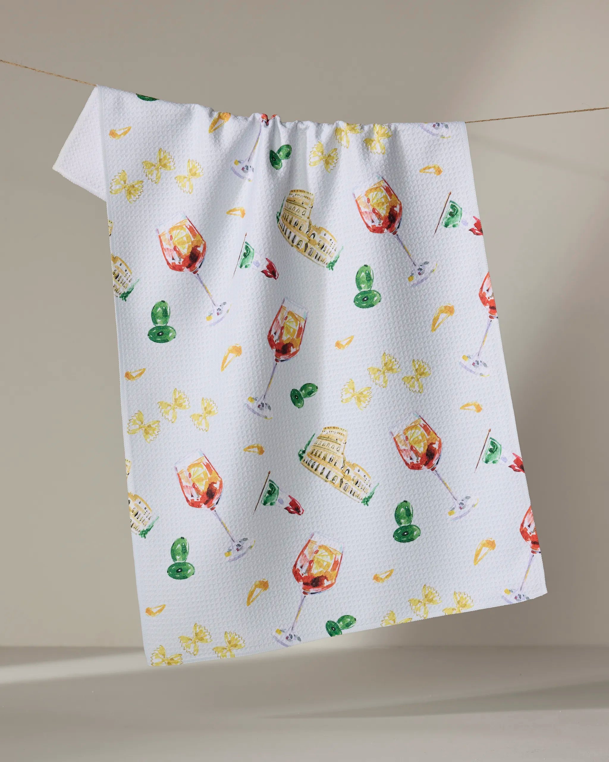 Aperol in Rome by Travel Write Draw features a white recycled kitchen towel adorned with colorful illustrations of wine glasses, the Colosseum, green olives, yellow pasta, and more Italian-themed motifs.