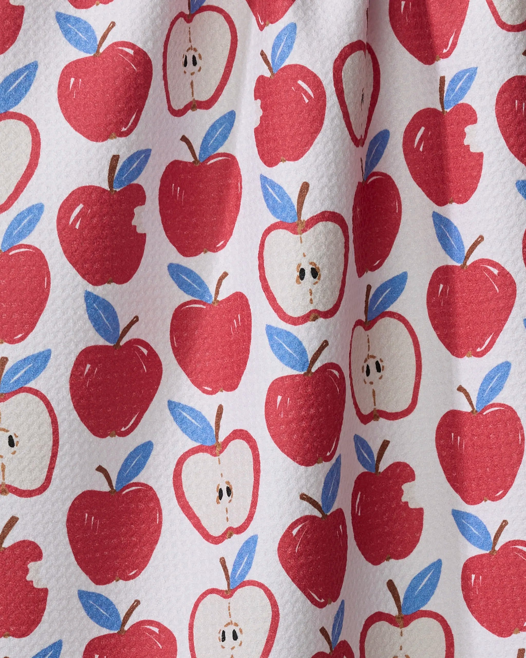 The "Apple A Day" tea towel by Hufton Studio features a repeating pattern of whole and halved red apples with green leaves on a white background. This absorbent kitchen towel is perfect for everyday use.