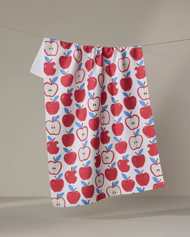 The Apple A Day tea towel by Hufton Studio features red apples and green leaves on white, hanging against a neutral background. Made from recycled materials, this absorbent towel brings eco-friendly charm to your kitchen.