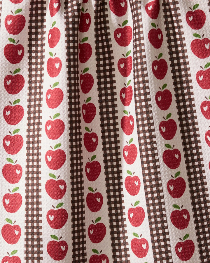 The Geometry “Apple Picking Day” tea towel features red apples with white highlights in vertical rows, alternating with brown plaid stripes on a textured white background for a charming, vintage country kitchen look.
