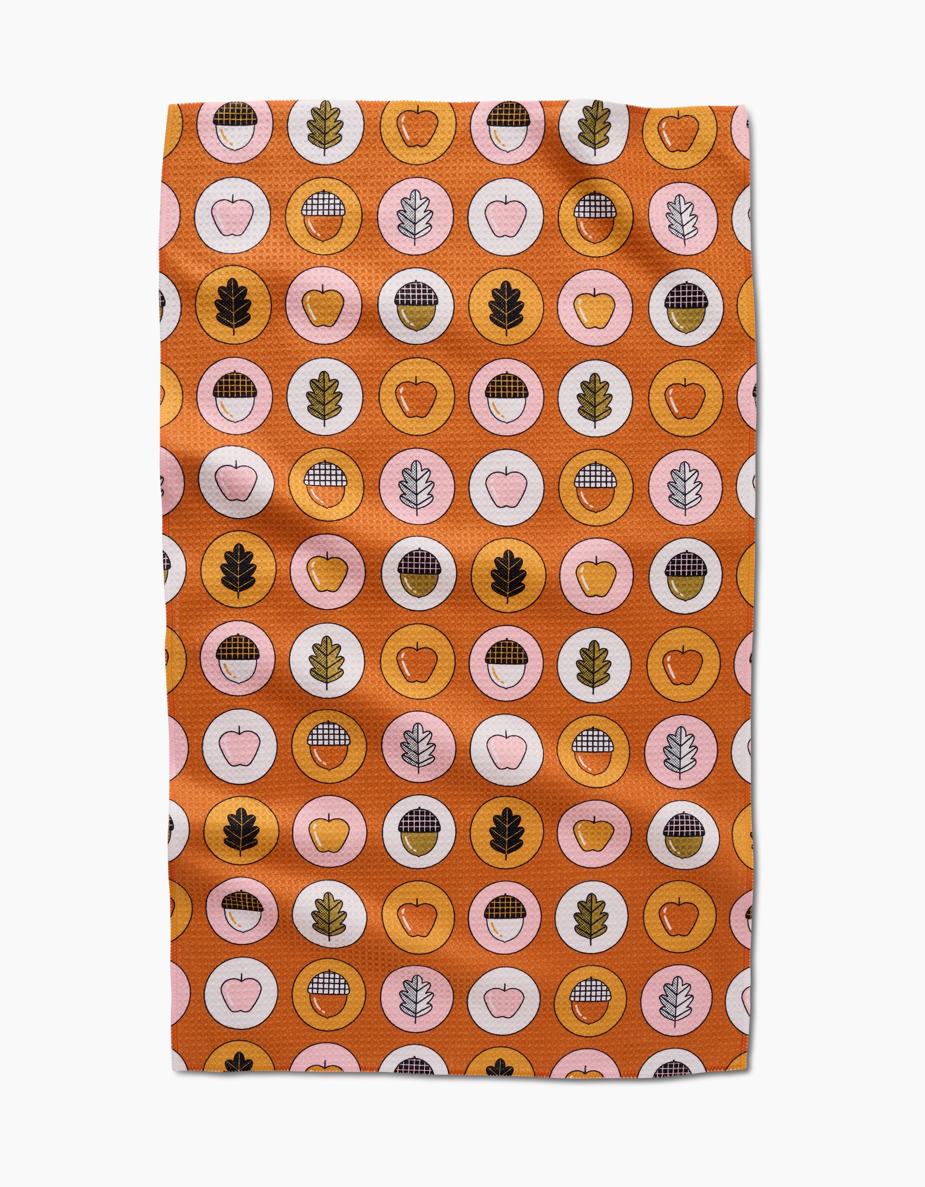 The Apples Acorns tea towel by Megan Roy is quick-drying and features a vibrant orange background with circles, apples, leaves, grid designs, and acorns in orange, pink, brown, and gold.