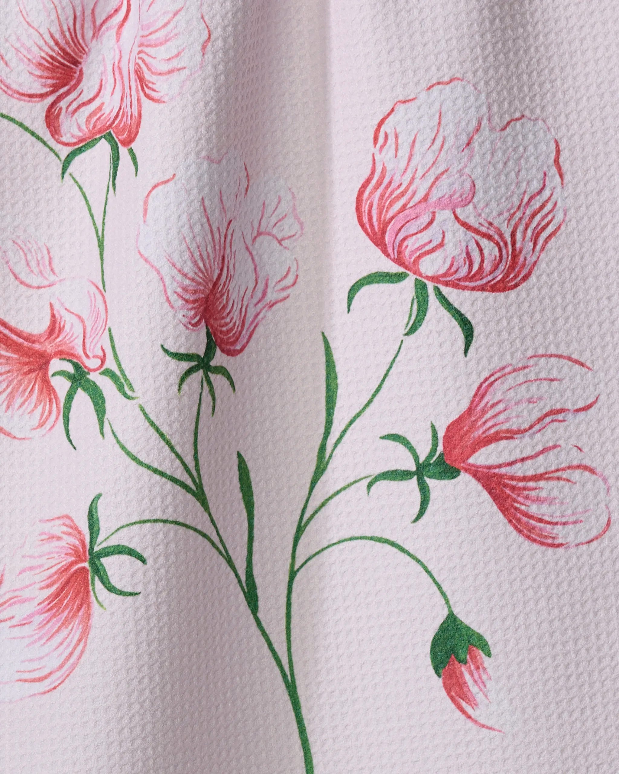 A close-up of the Linda Fox "April Sweet Pea" tea towel made from recycled materials, featuring textured fabric with pink and red floral prints and green leaves on a light pink background.