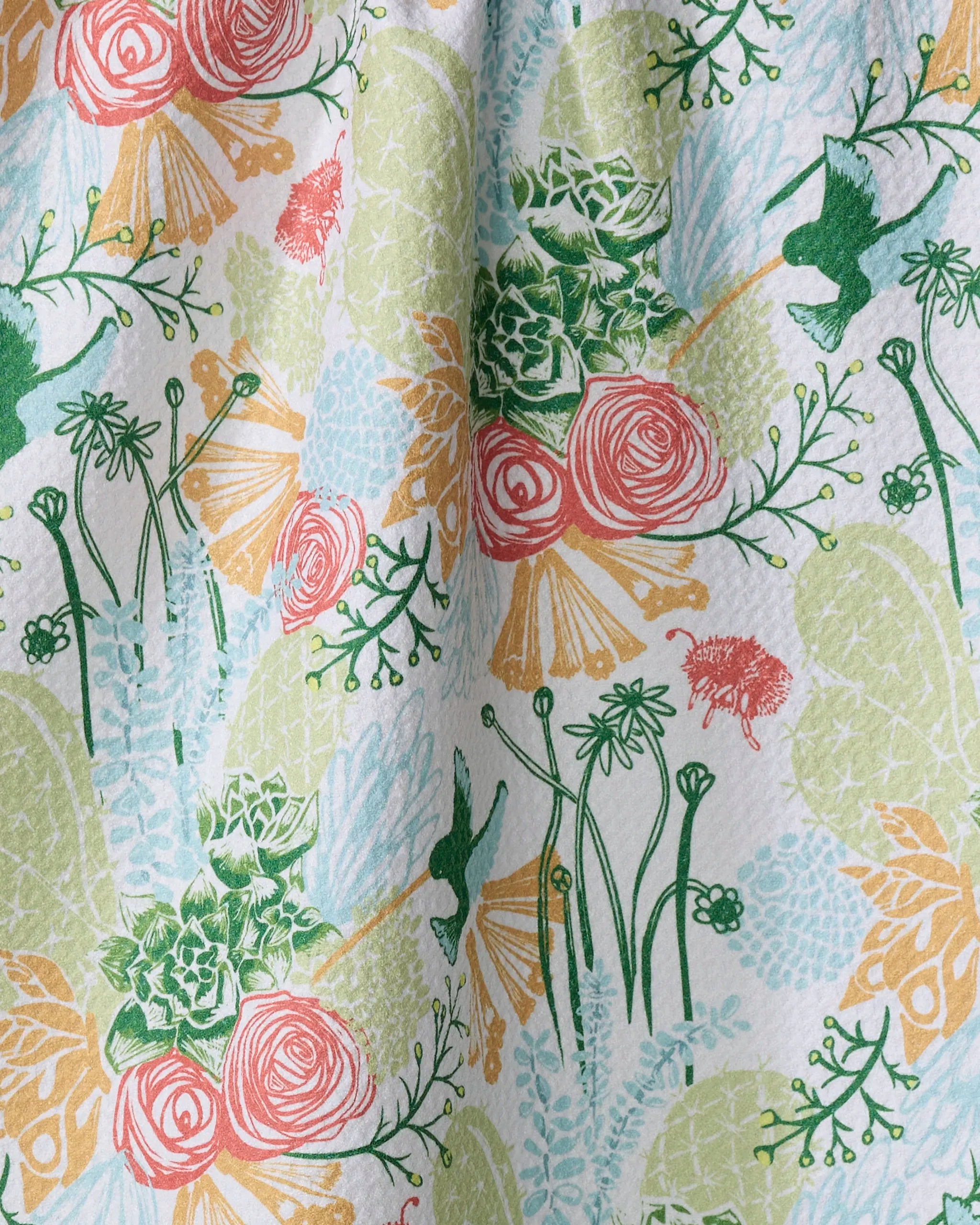 The “Arizona Spring” kitchen towel by Elisabeth Wing features green leaves, pink roses, succulents, yellow flowers, and blue hummingbirds on a pastel background—made from recycled materials for an eco-friendly touch.