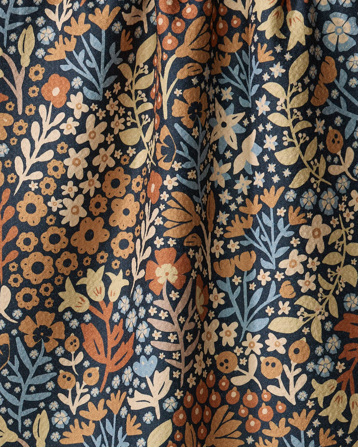The Arthur towel by Danelys Sidron features a dense floral pattern in orange, yellow, and blue on a dark background. Ultra-absorbent with gathered folds, its visible texture is enhanced by deep shadows.
