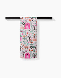 The Asher tea towel by Amy MacCready, made from recycled materials, displays vibrant barns, trees, flowers, chickens, tractors, and gardening tools and hangs neatly on a black horizontal towel bar.