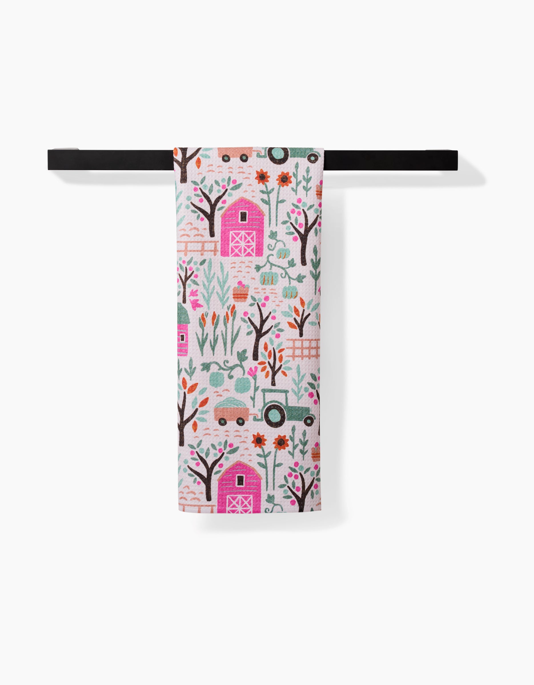 The Asher tea towel by Amy MacCready, made from recycled materials, displays vibrant barns, trees, flowers, chickens, tractors, and gardening tools and hangs neatly on a black horizontal towel bar.