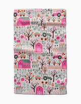The Asher tea towel by Amy MacCready features whimsical pink barns, tractors, trucks, trees, flowers, and animals in green, pink, orange, and brown. Ultra-absorbent fabric with a lightly wrinkled texture.