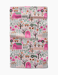 The Asher tea towel by Amy MacCready features whimsical pink barns, tractors, trucks, trees, flowers, and animals in green, pink, orange, and brown. Ultra-absorbent fabric with a lightly wrinkled texture.