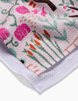 A close-up of the Asher tea towel by Amy MacCready features a colorful floral pattern with pink, orange, and green motifs. The folded corner reveals its textured white underside, showcasing an ultra-absorbent design.