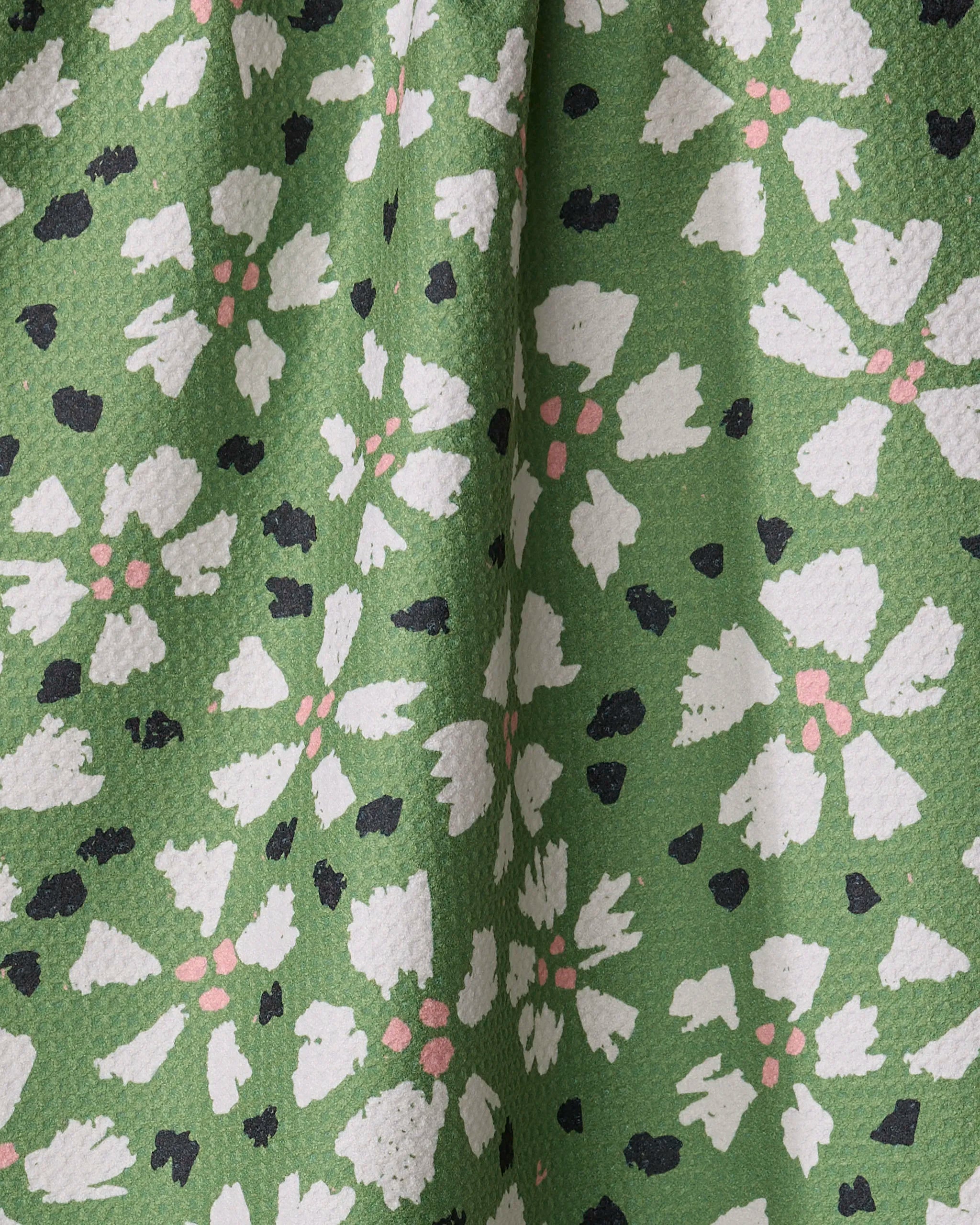 The Aster towel by Kayla Ann features green textured fabric with white flowers, pink centers, and black dots. Quick-drying and slightly draped, it's perfect as an eco-friendly tea towel for your kitchen.