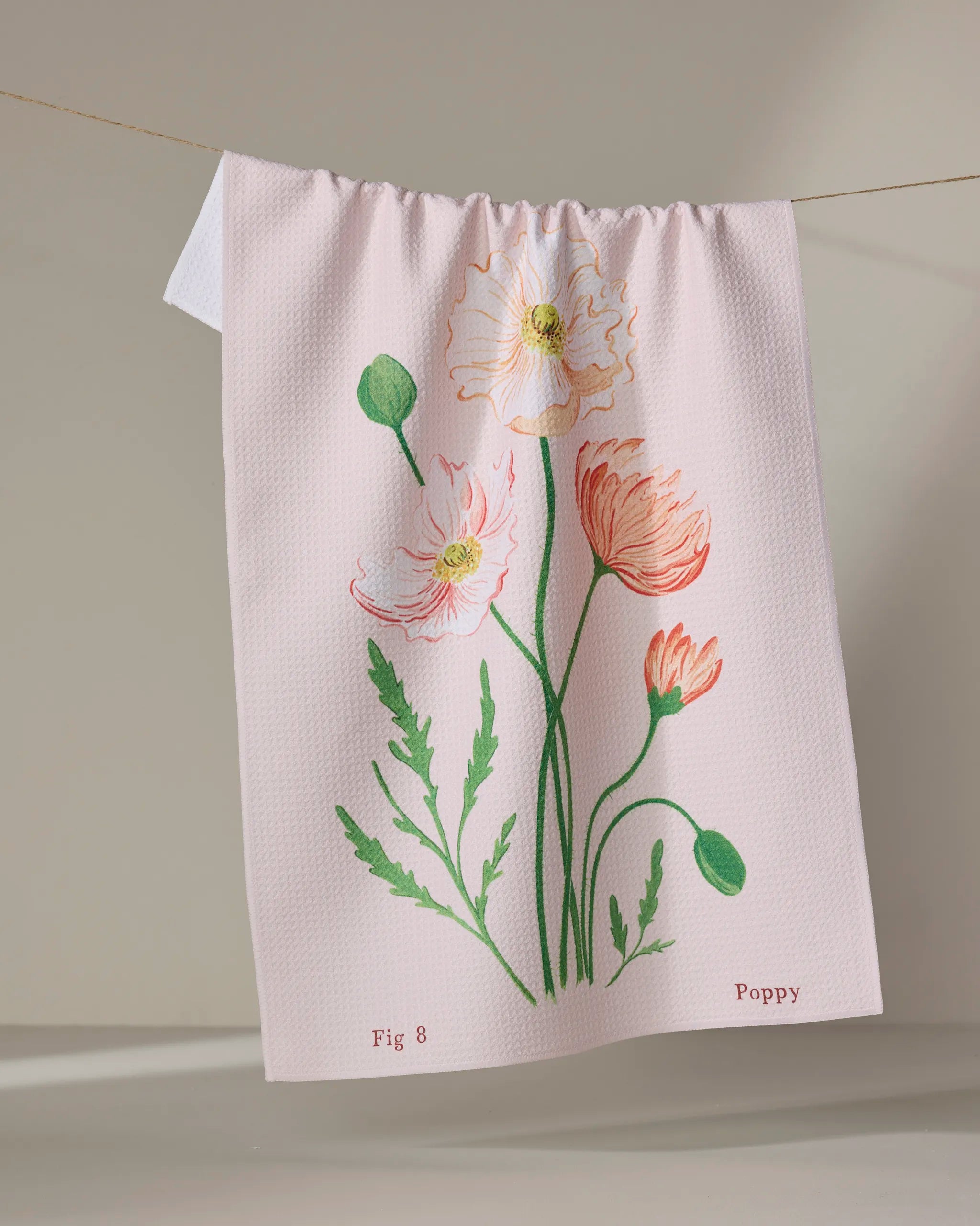 The August Poppy kitchen tea towel by Linda Fox is pale pink, made from recycled materials, and features a botanical poppy illustration in green, red, and white. "Fig 8" and "Poppy" are printed in the bottom corners.