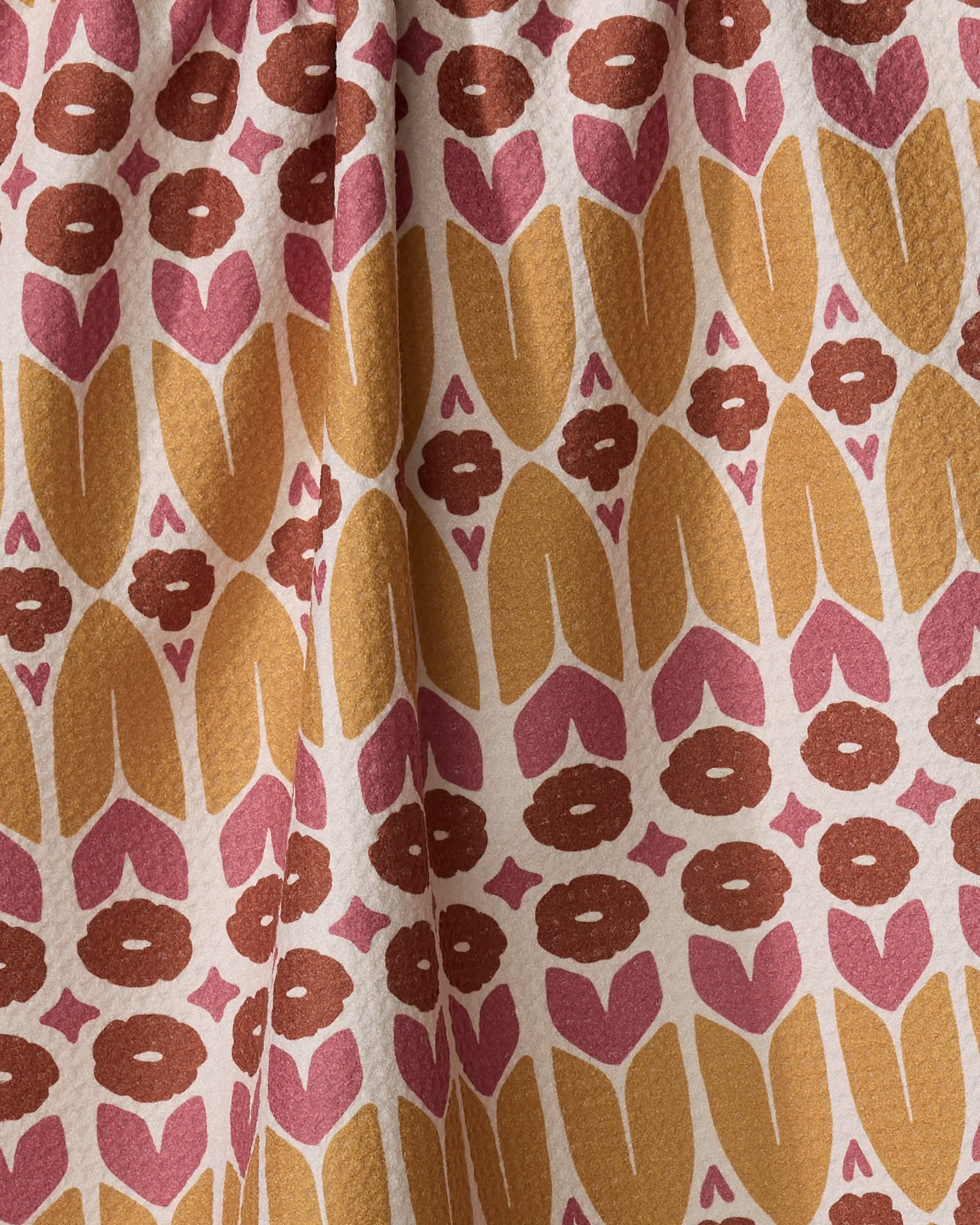 A close-up of Kayla Ann's "Autumn Groove" tea towel shows a bold, abstract floral design with stylized tulip shapes in mustard yellow, pink, and brown on a textured, recycled-material background.