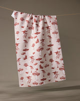 The Geometry Autumn Mushrooms tea towel, made from recycled materials and featuring a red mushroom and animal pattern, hangs on a string against a neutral background.